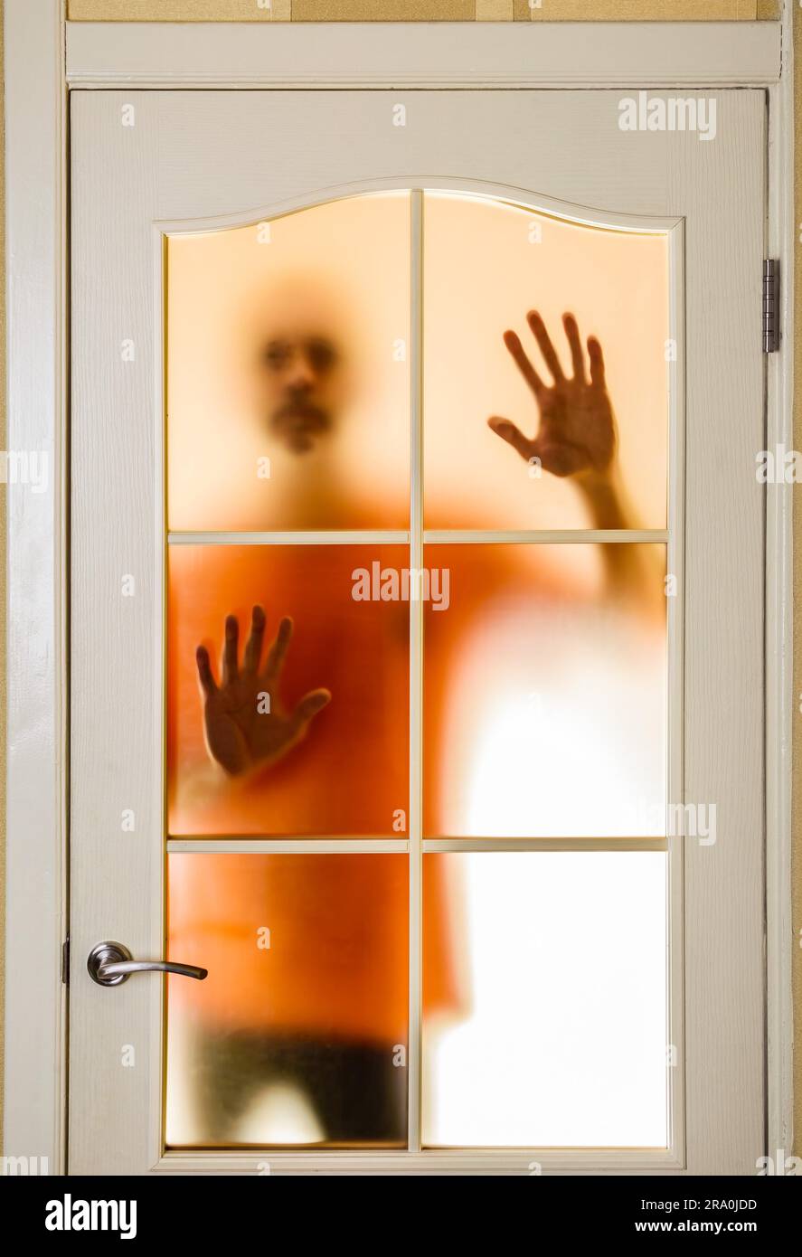 Silhouette von einem unbekannten Mann in Orange gesehen hinter einer verschlossenen Glastür, wie ein Geist oder ein Ausländer Stockfoto