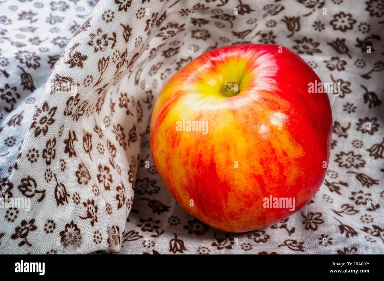 Einen schönen roten und gelben Apfel auf einem geblümten Stoff unter der Sonne Stockfoto