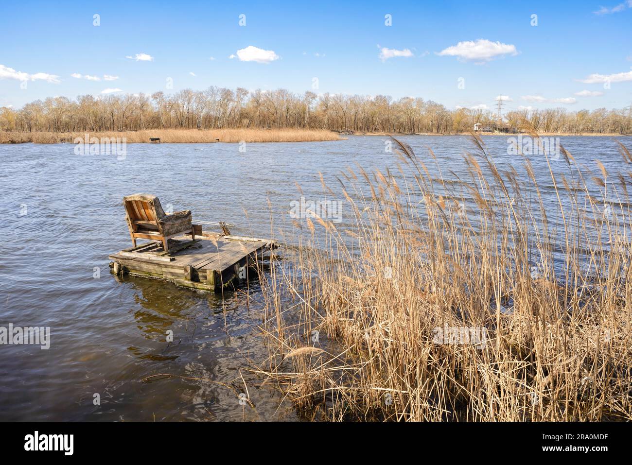 Ein komfortabler Sessel auf einem Ponton wartet auf einen Fischer auf dem See. Die Wolken laufen am blauen Himmel, vom Wind geschoben Stockfoto