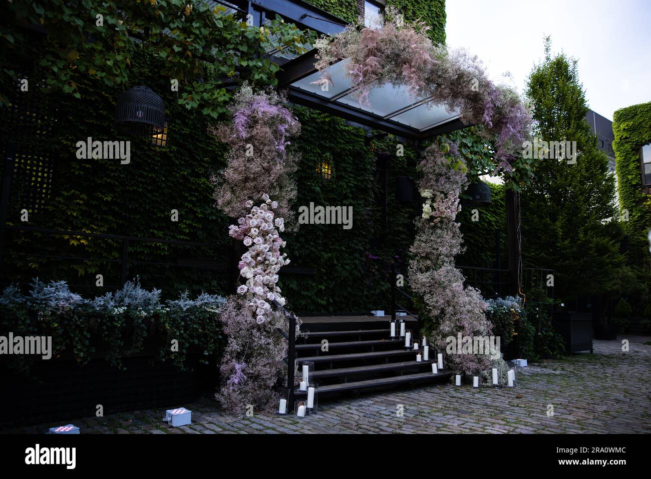 Wunderschöne Blumenarrangements mit Blumenstrauß-Hochzeit mit Rosen, Kerzen und dem Atem des Babys in einem üppigen botanischen Garten mit Treppe und Bogen. Stockfoto