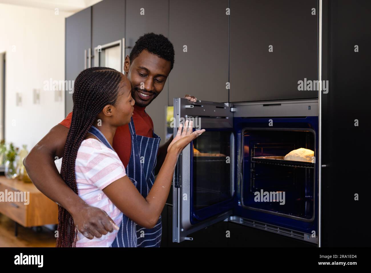 Glückliches afroamerikanisches Paar in Schürzen, das Brot im Ofen in der Küche backt Stockfoto