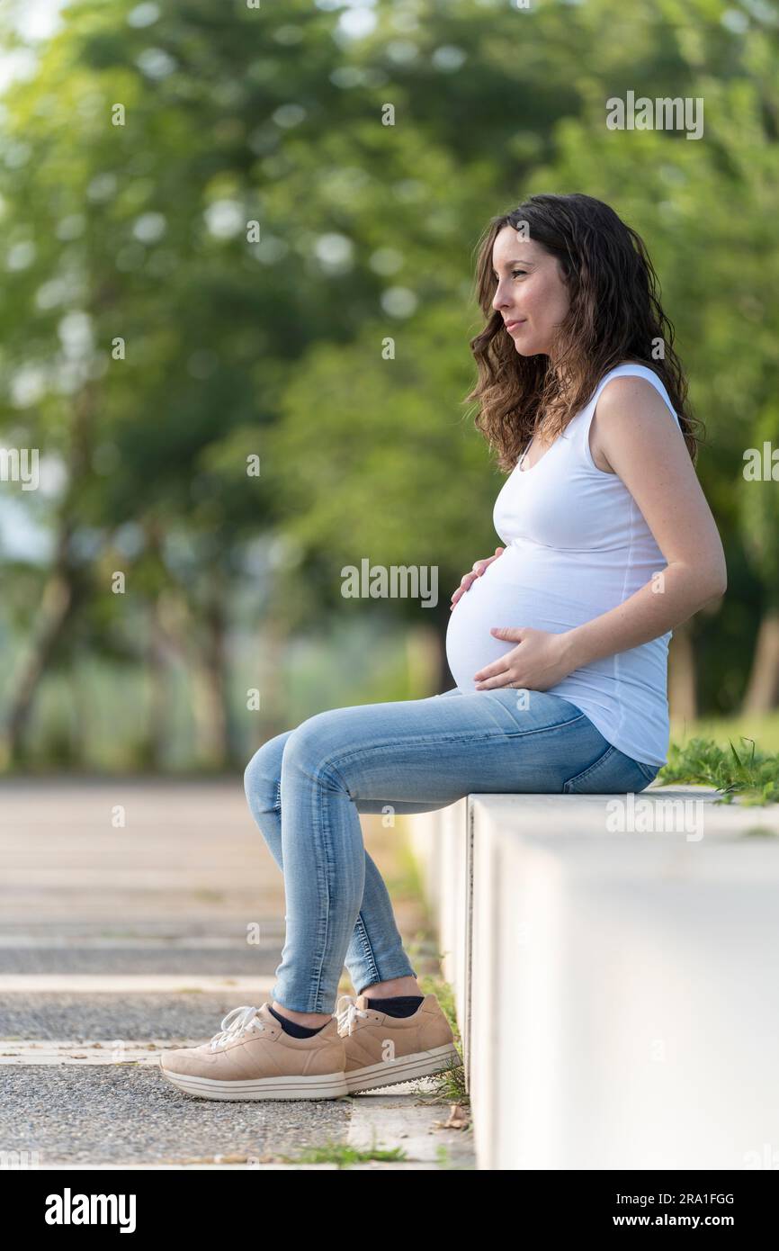 Junge schwangere Frau, die auf der Straße auf ihrem Bauch sitzt Stockfoto