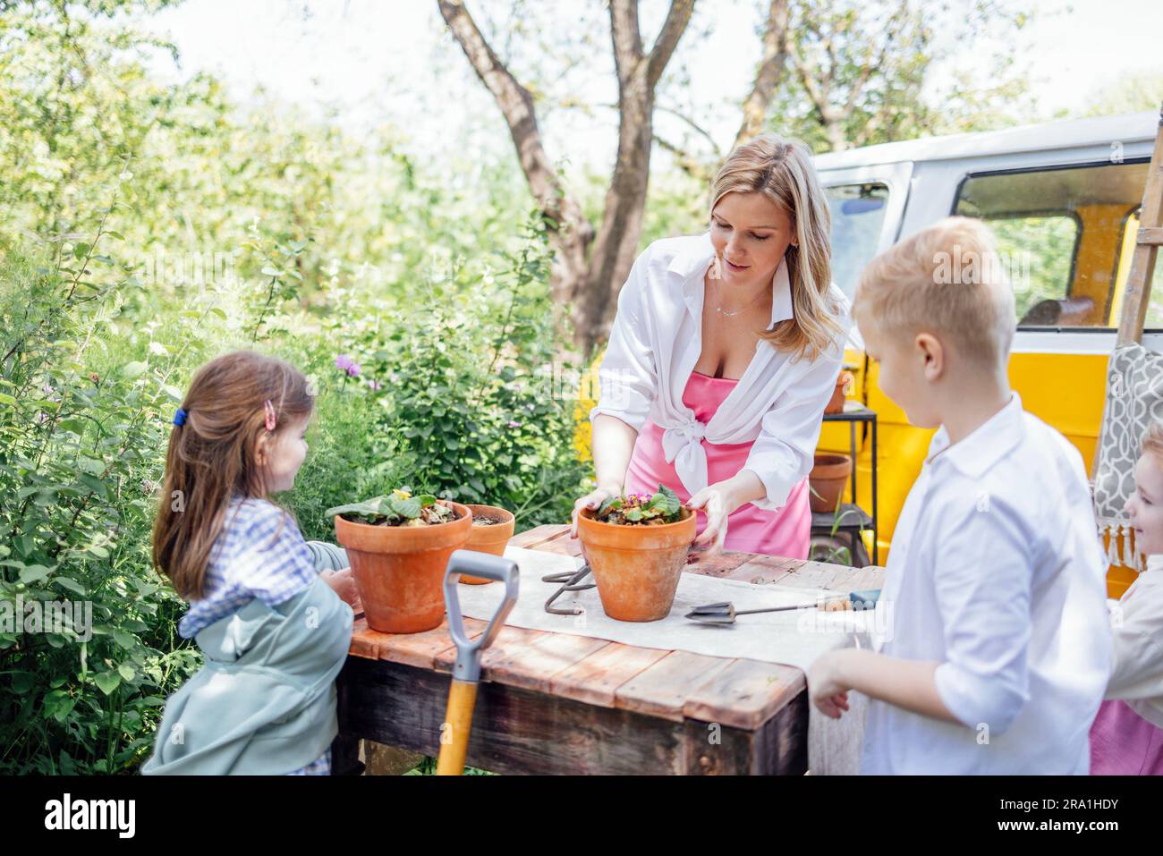Eine junge Frau und ihre drei Kinder Pflanzen Blumen in Töpfen im Garten. Hübsche Mutter, süße Mädchen und Junge sind im Gartenbau beschäftigt. Glückliche Familie Stockfoto