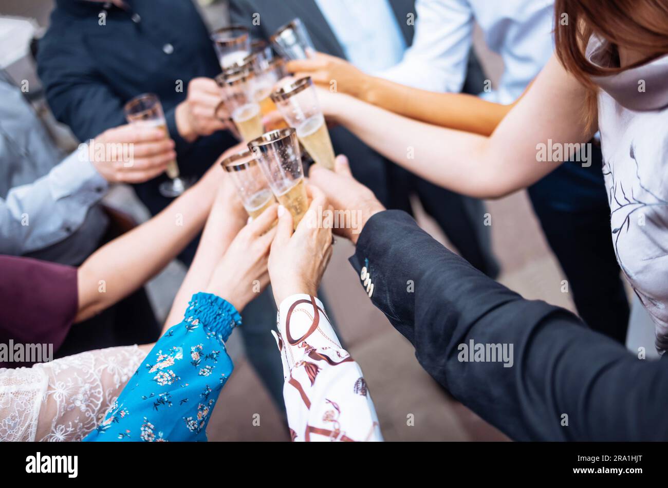 Weibliche und männliche Hände halten elegante, langstielige Gläser Champagner und klopfen sie zusammen. Feierlicher Toast mit Sekt im Freien. Geburtstag Stockfoto