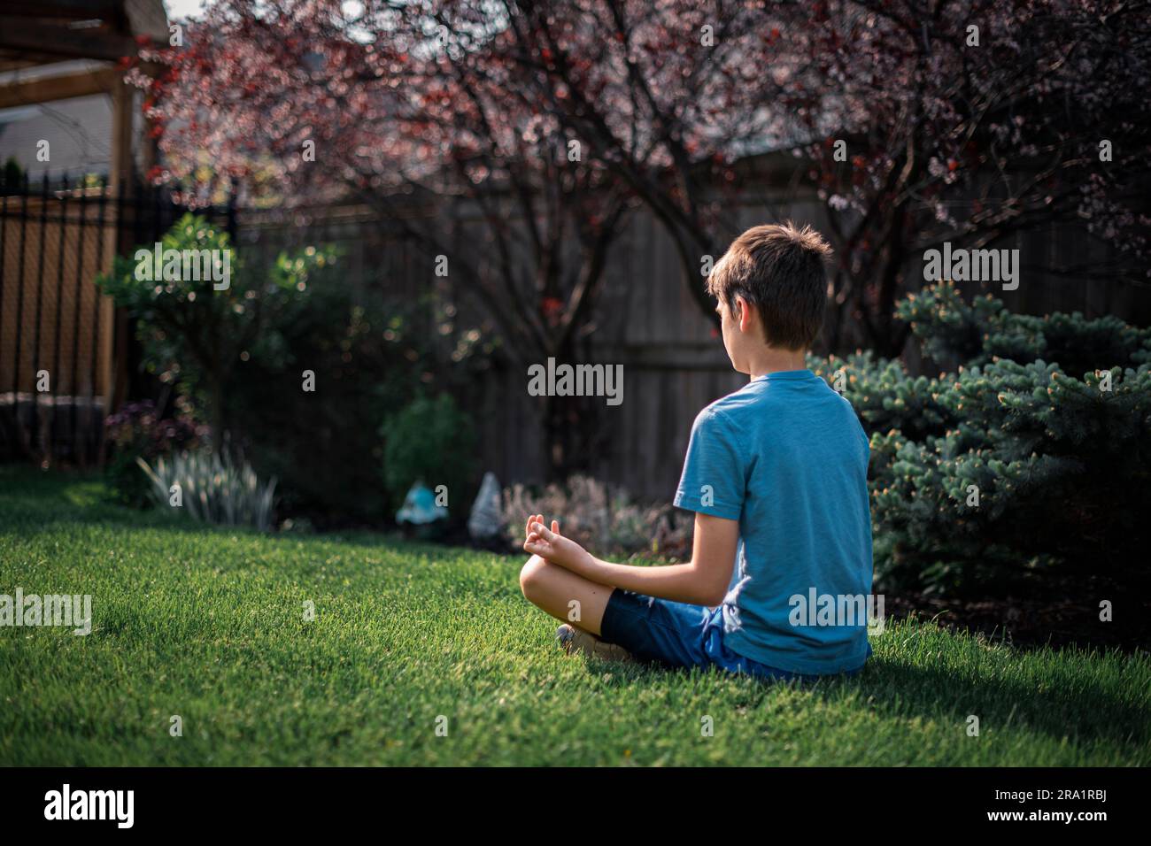 Rückblick auf einen Tween-Jungen, der auf dem Rasen im Garten meditiert. Stockfoto