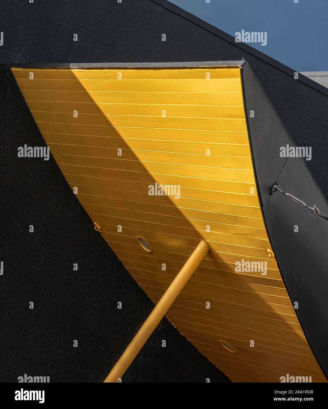 Abstraktes Bild einer gelben Holztafel und einer schwarzen Wand vor einem blauen Himmel. Vertikales Format. Stockfoto