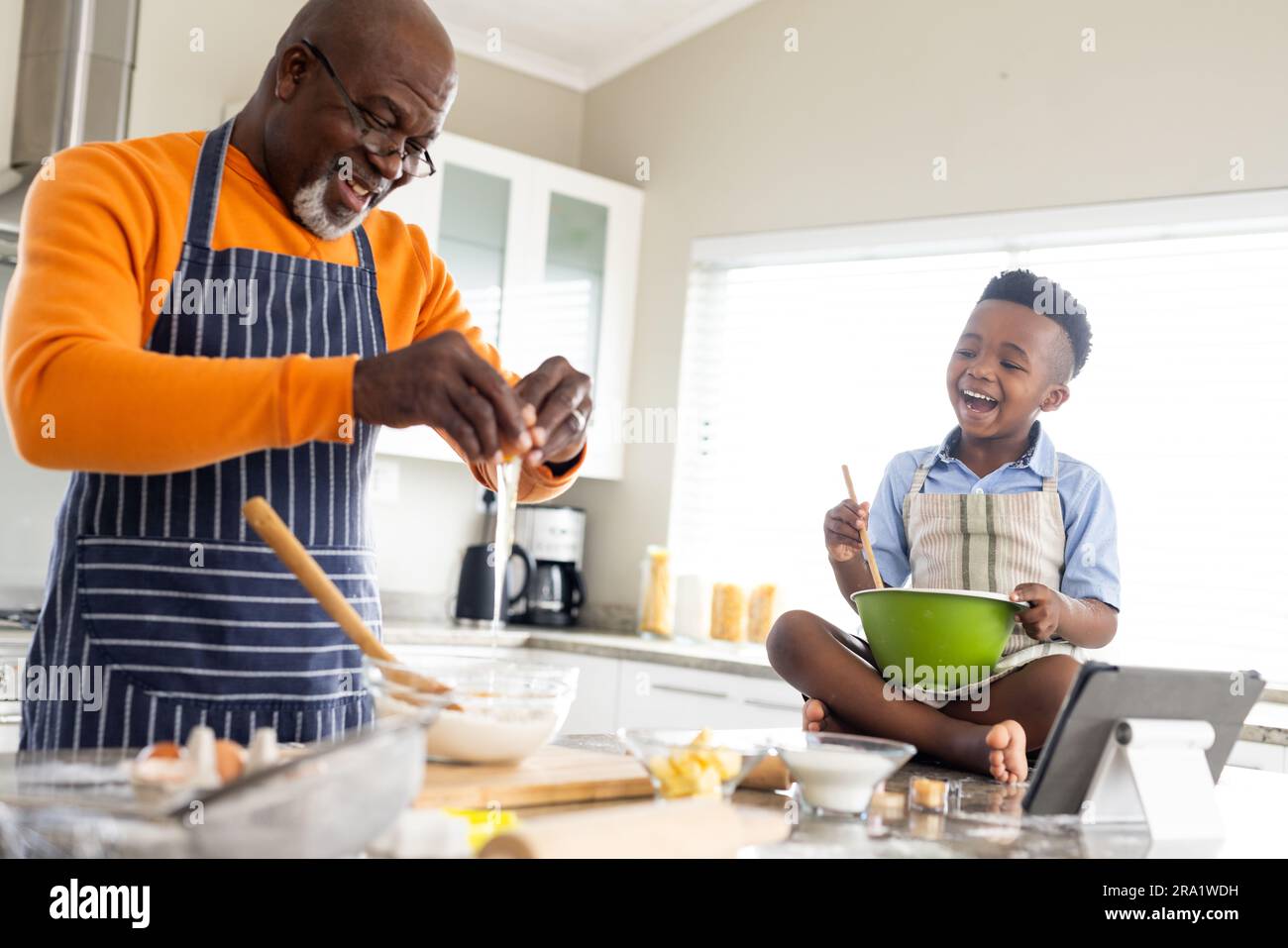 Fröhlicher afroamerikanischer Großvater und Enkel, die in der Küche backen, Zeitlupe Stockfoto