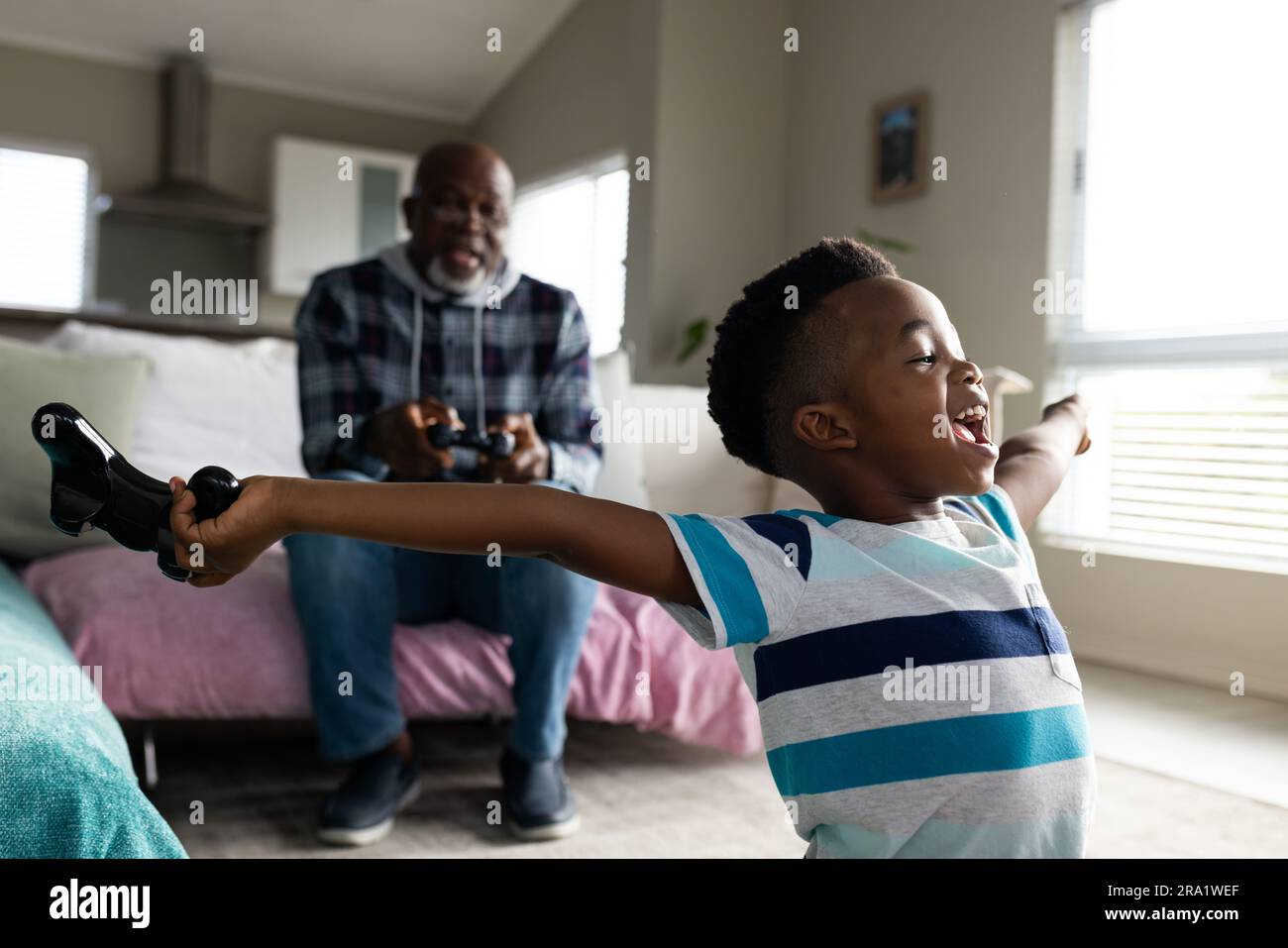 afroamerikanischer Großvater und Enkel sitzen auf dem Sofa und spielen Videospiele Stockfoto