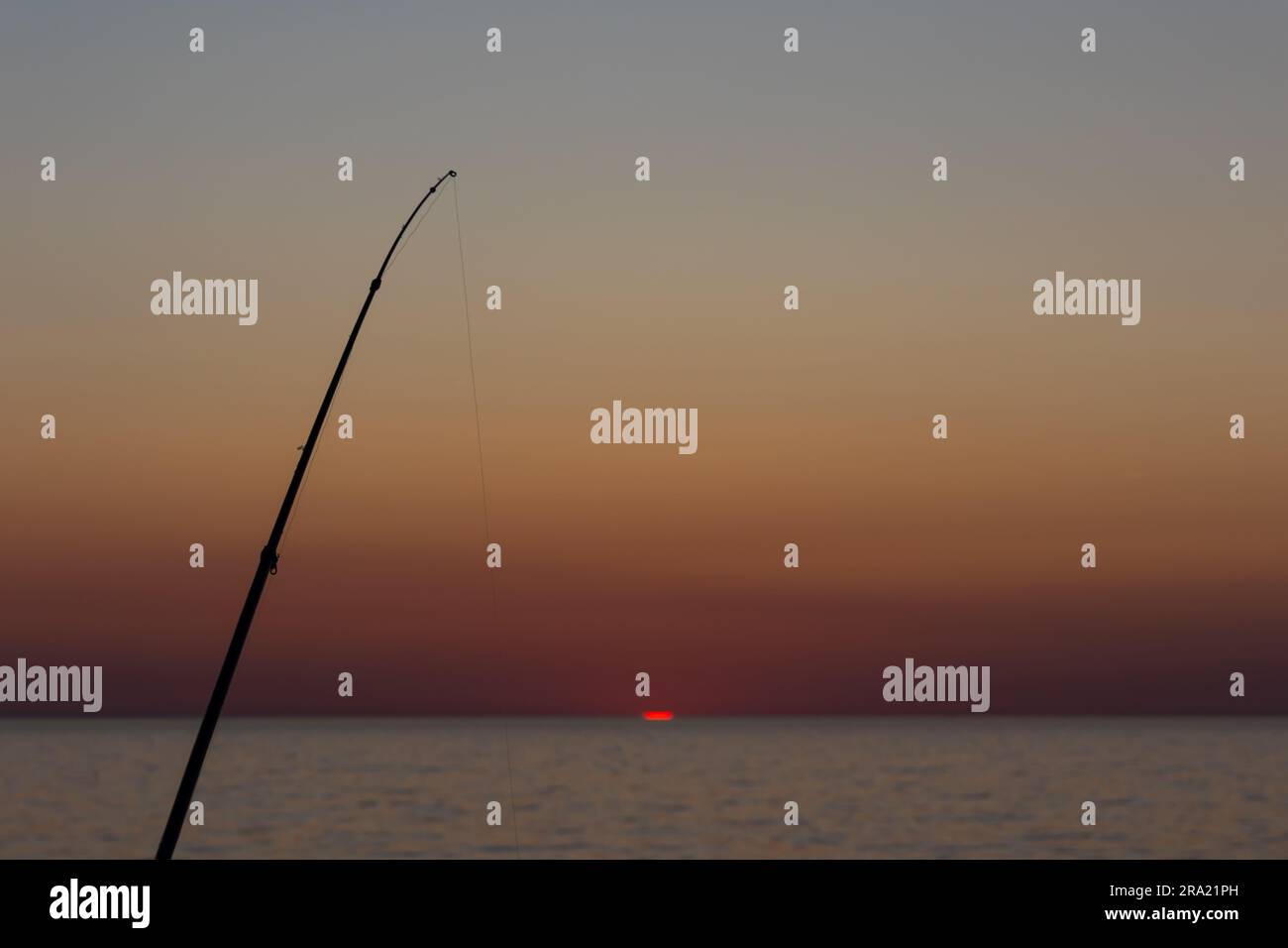 Die Silhouette einer Angelrute vor dem Hintergrund der untergehenden Sonne. Statische Aufnahme während eines wolkenlosen Abends Stockfoto