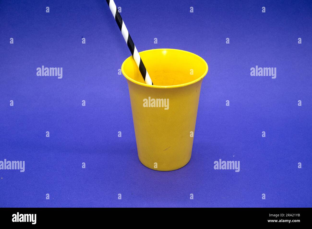 Hellgelber Trinkbecher aus Kunststoff auf blauem Hintergrund mit gestreiftem Trinkhalm Stockfoto