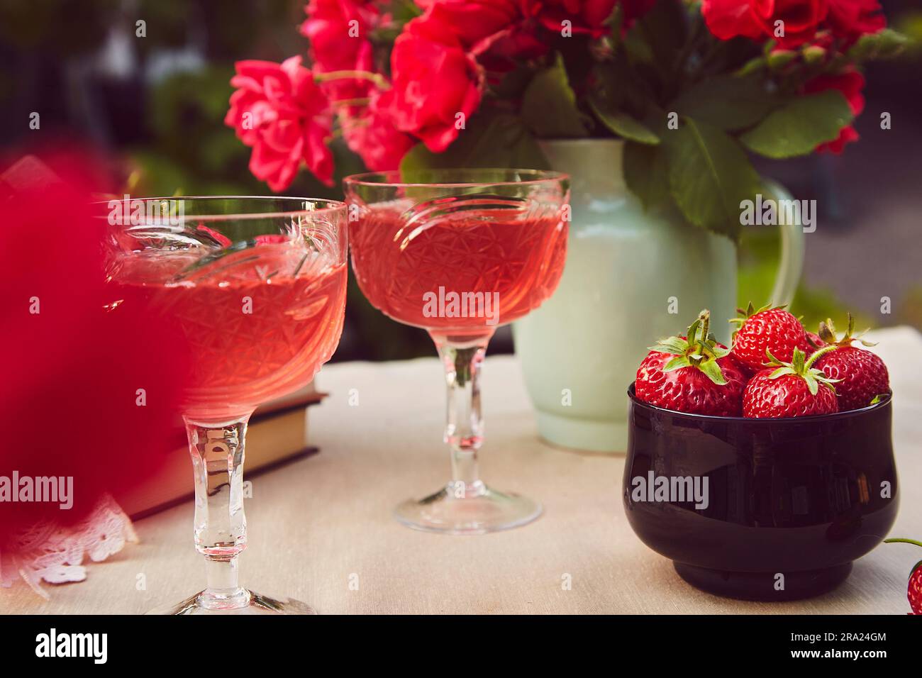 Gemütliche ästhetische Tischgestaltung. Ein paar Gläser mit roter hausgemachter Erdbeer-Infusion, Wein. Rosenstrauß. Stockfoto