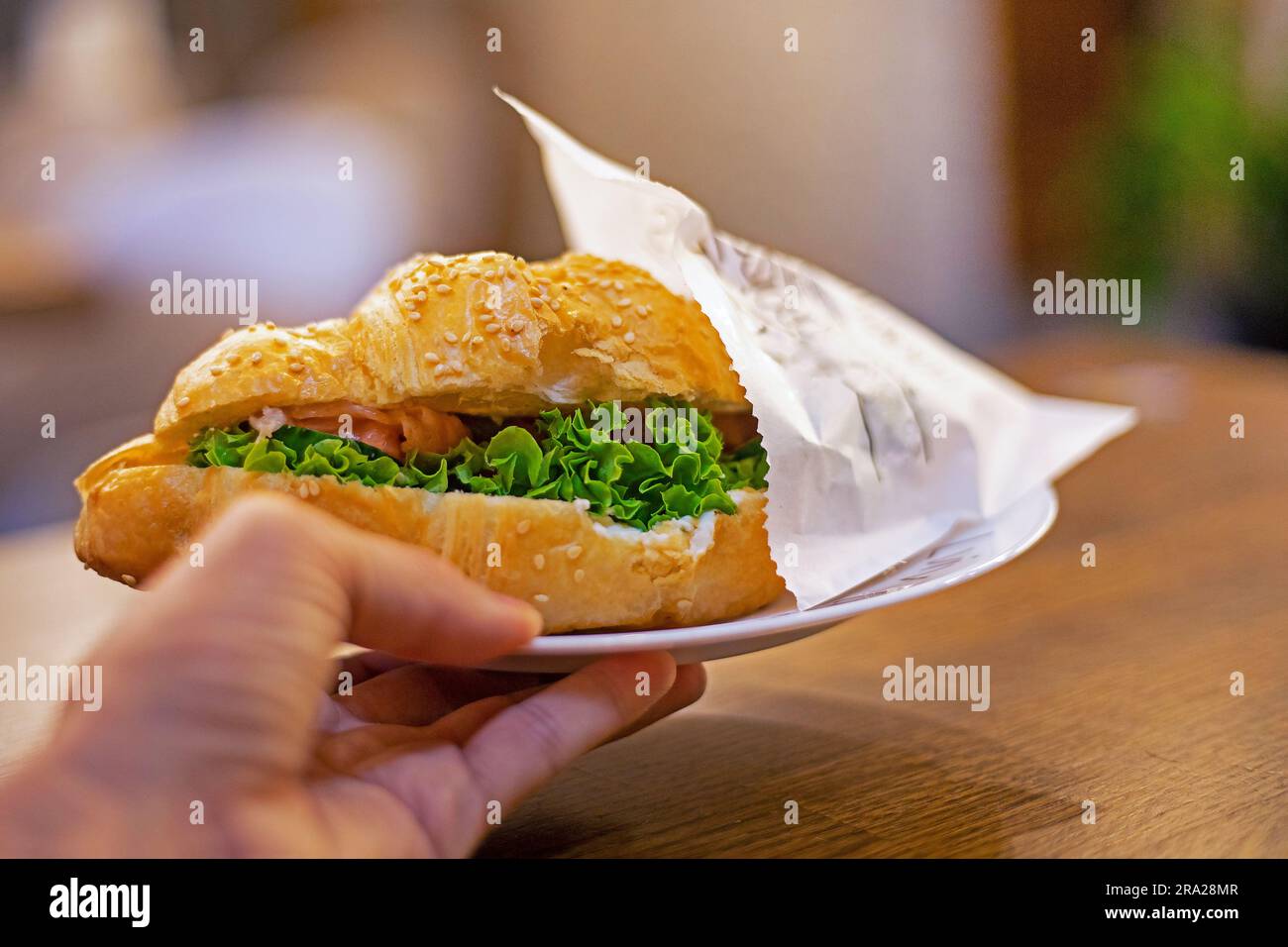 Halten Sie einen Teller mit frischem Croissant mit Lachs, Salat und philadelphia in den Händen. Bäckerei Stockfoto