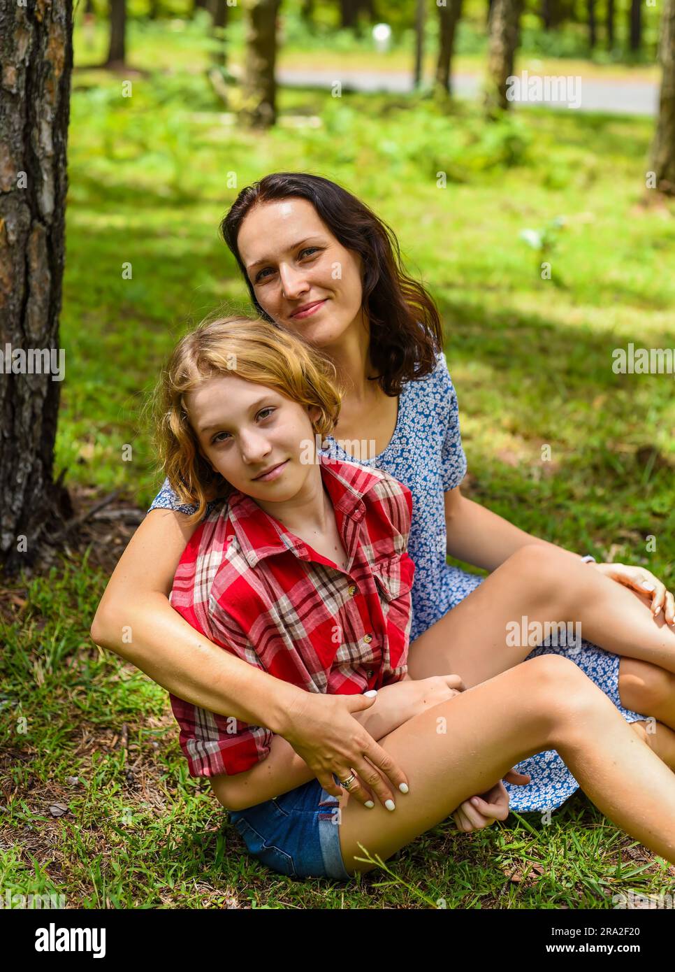 Mutter umarmte ihre kleine Tochter und ruhte sich auf ihrem Schimmer gegen grünes Gras im Wald aus Stockfoto