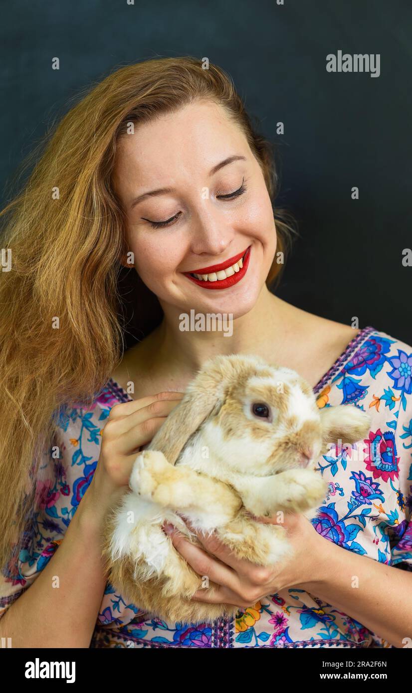 Eine wunderschöne russin mit langen blonden Haaren, die ein Kaninchentier in der Hand an die schwarze Wand hält Stockfoto