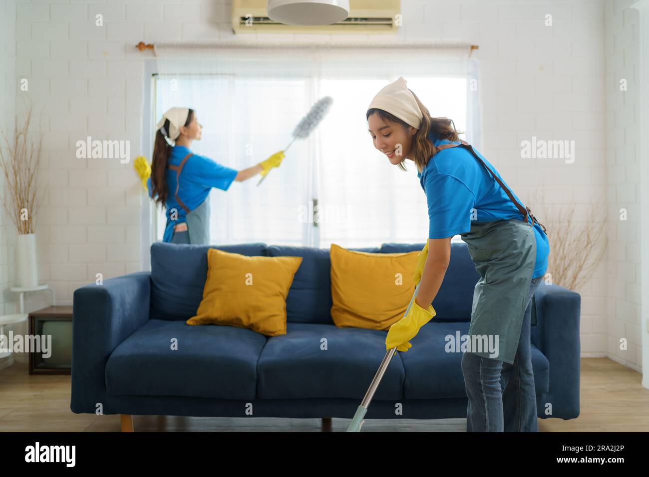 Zwei fleißige asiatische Zimmermädchen arbeiten nahtlos zusammen und reinigen das Wohnzimmer mit Präzision und Effizienz, sodass sie bei ihrer Suche keine Ecken unberührt lassen Stockfoto