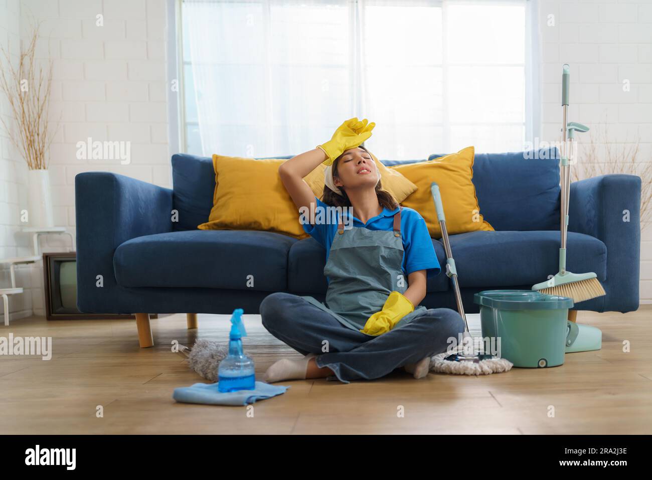 Das erschöpfte asiatische Zimmermädchen kämpft mit Ermüdung, während es das Haus wischte, und zeigt die Herausforderungen und harte Arbeit hinter dem Haus Stockfoto