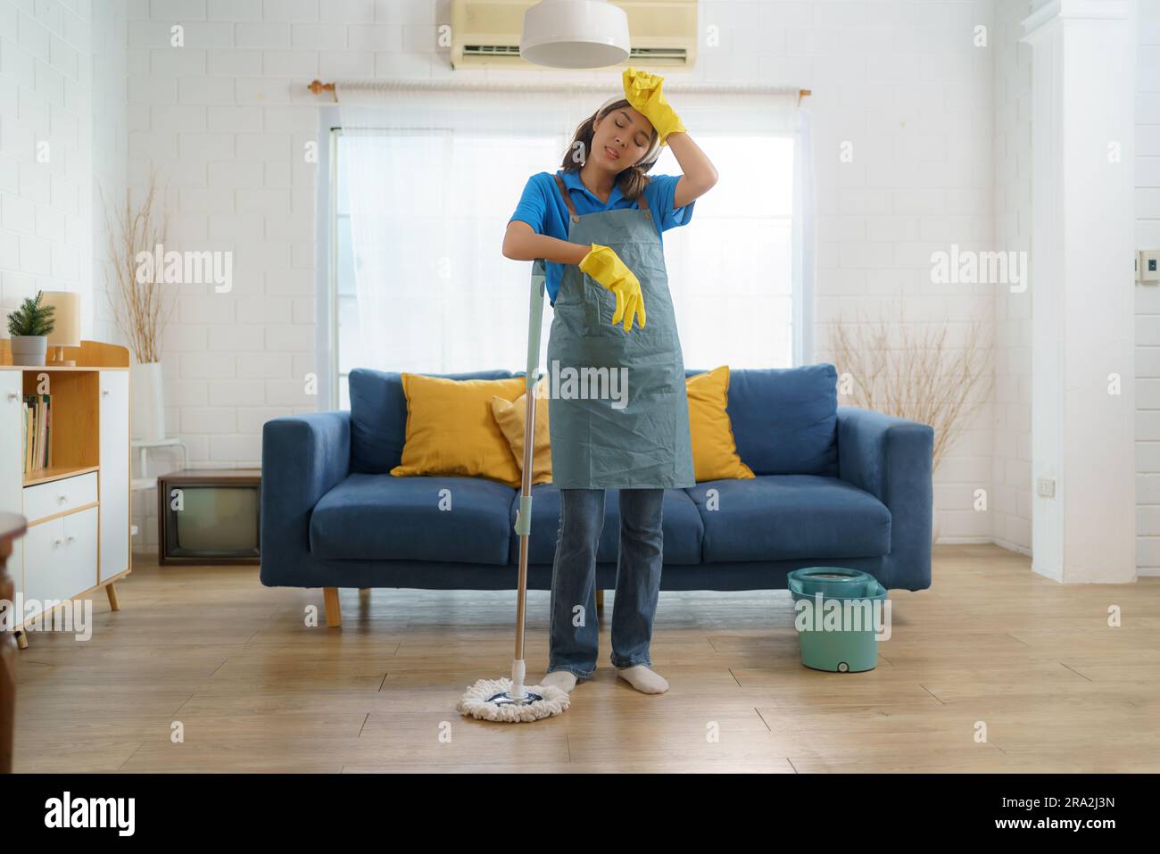 Das erschöpfte asiatische Zimmermädchen kämpft mit Ermüdung, während es das Haus wischte, und zeigt die Herausforderungen und harte Arbeit hinter dem Haus Stockfoto