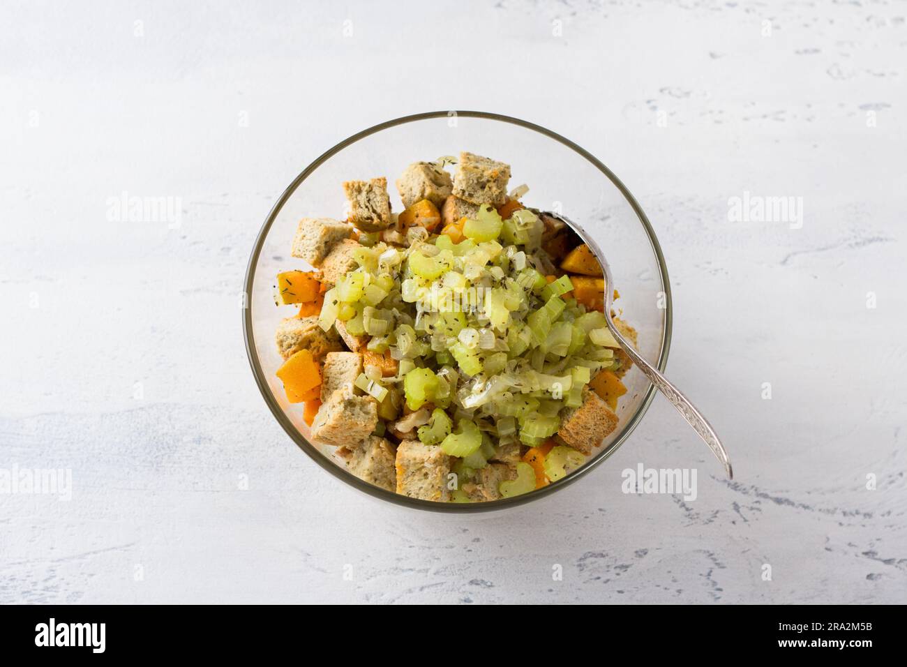 Eine Glasschüssel mit einer Mischung aus Kürbiswürfeln, Croutons, Sellerie mit Zwiebeln und Gewürzen auf hellblauem Hintergrund, Draufsicht. Phase des Kochens de Stockfoto