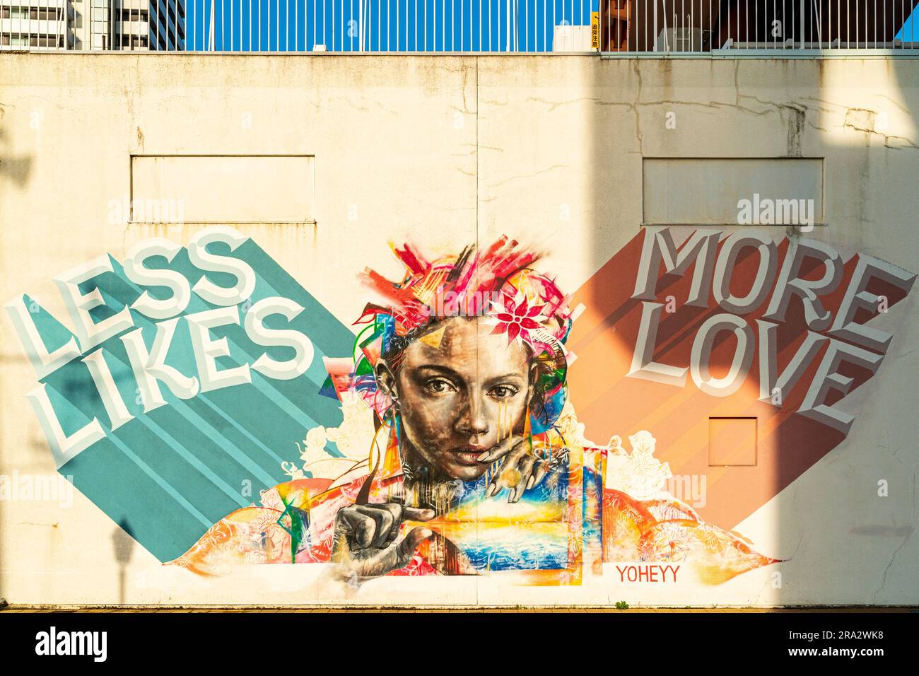 Wandgemälde des Osaka-Künstlers Yoheyy, „Less Likes, More Love“ an einer Lagerwand im Meriken Park am Ufer von Kobe, Japan. Goldene Stunde. Stockfoto