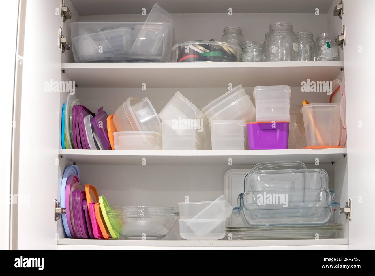 Offener Küchenschrank mit Kunststoff- und Glasbehältern im Inneren. Stockfoto