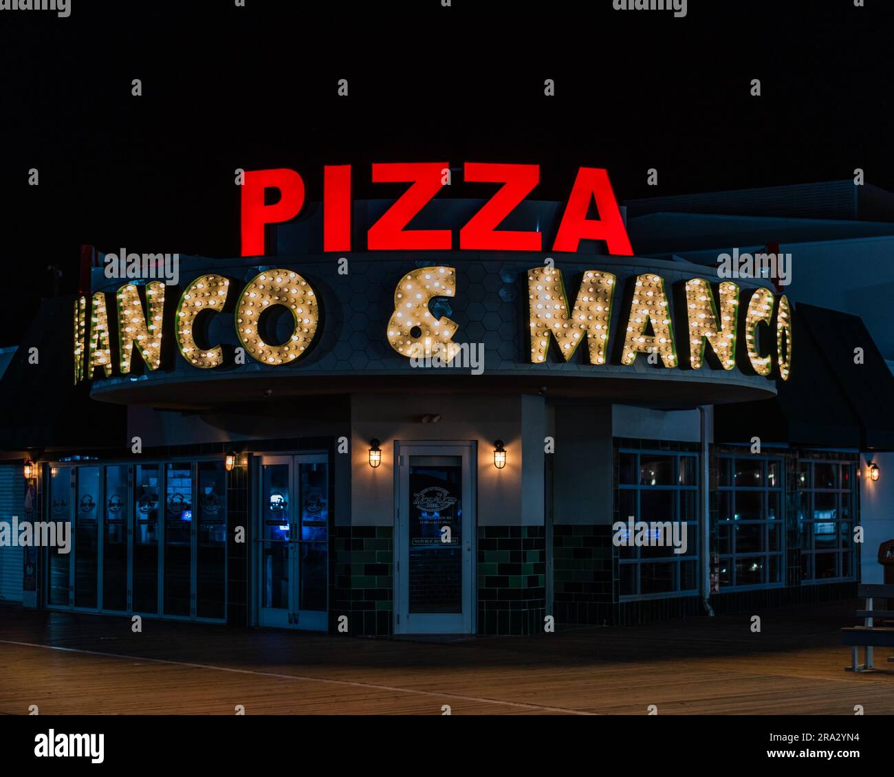 Blick von außen auf das Pizzarestaurant Manco & Manco bei Nacht, beleuchtet von der hellen Außenbeleuchtung Stockfoto