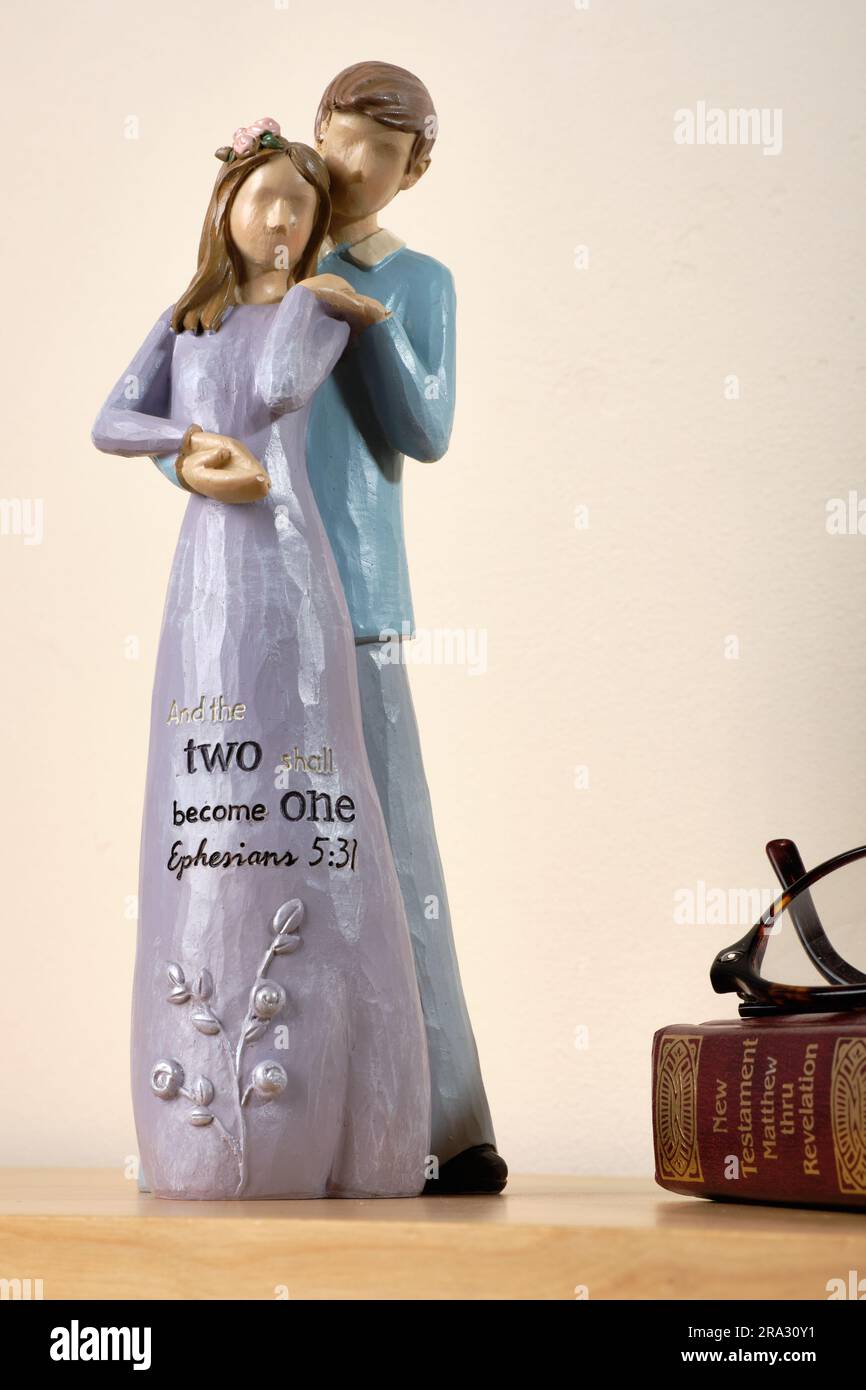 Keramikverzierung eines liebevoll stehenden Mannes und einer liebevoll stehenden Frau. Das Frauenkleid ist lila und mit der Inschrift "und die beiden werden ein Ephesier 5:31" versehen. Stockfoto