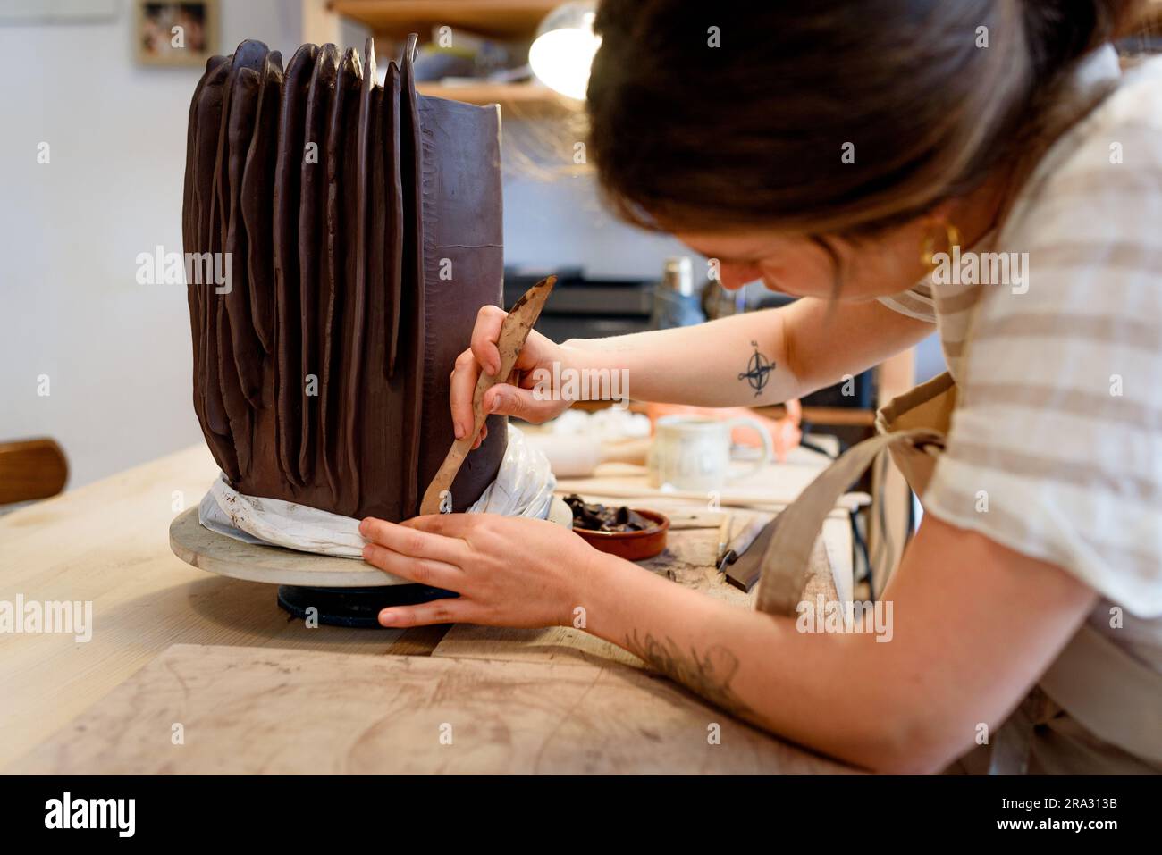 Eine Frau in einer Töpferwerkstatt, die rohe Keramikvase und Lehm bearbeitet, um Gras zu machen. Keramikwerkstatt mit natürlichem Licht zum Schaben, Glätten, Formen und Formen Stockfoto