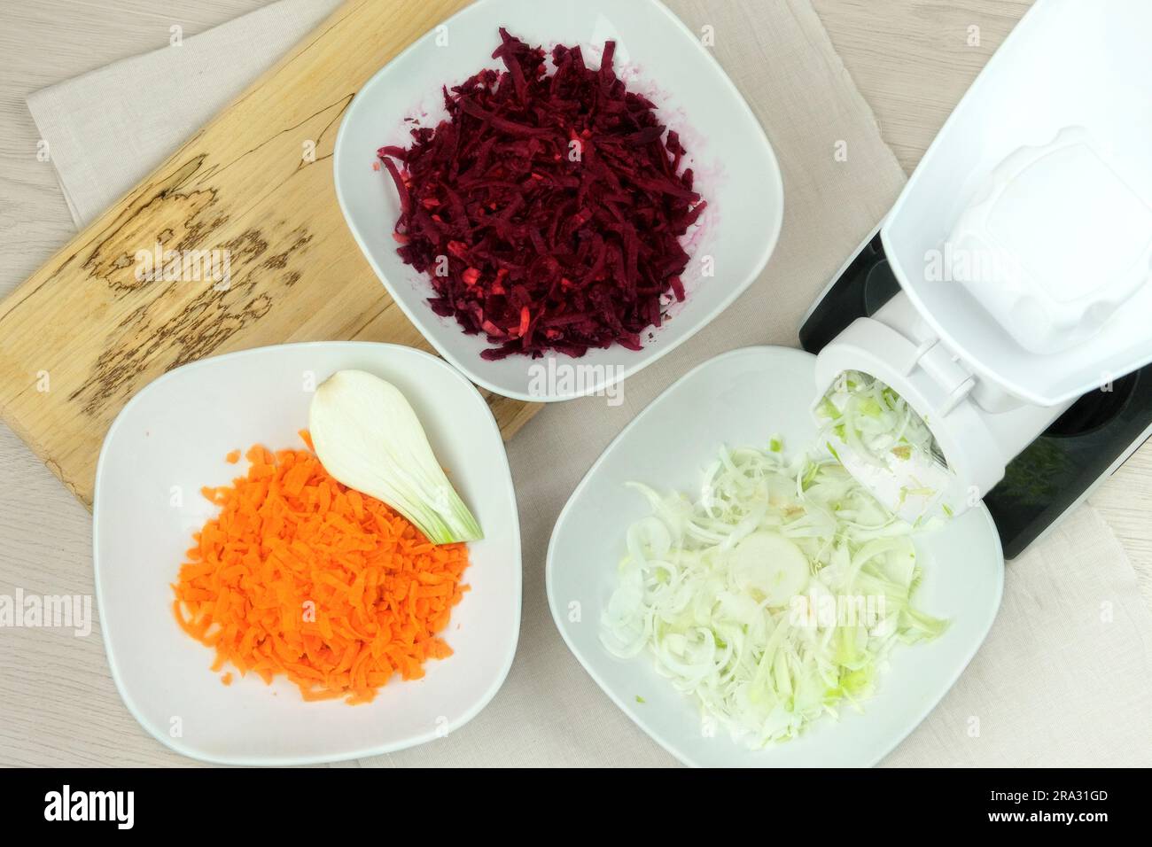 Karotten, Rüben und Zwiebeln in einem Gemüseschneider auf dem Küchentisch. Gehacktes Gemüse fällt in eine Schüssel. Hausgemachte gesunde Lebensmittel. Stockfoto