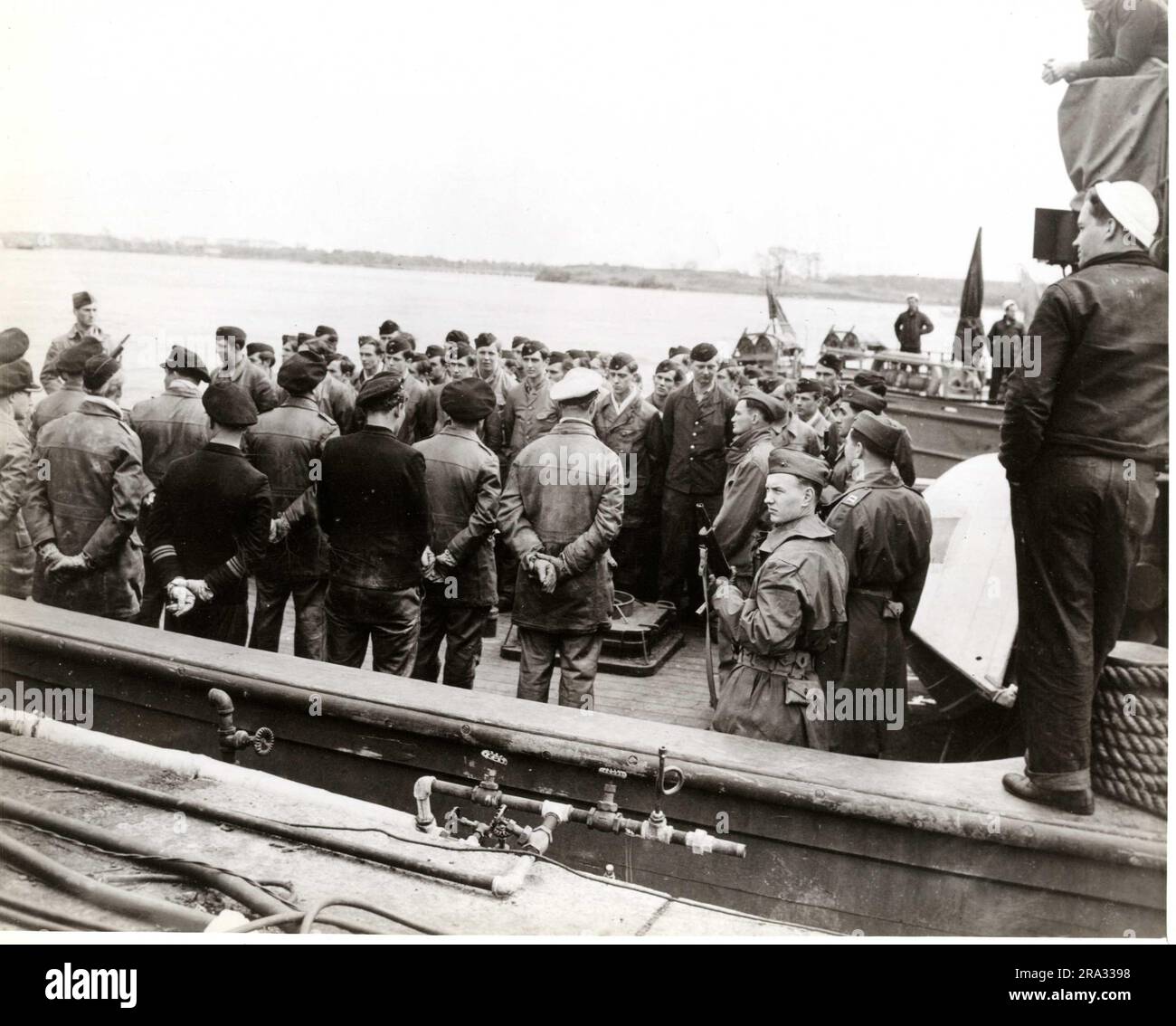 Deutsche Gefangene von U-873 am Marinehafen Portsmouth in New Hampshire. Dieser Artikel besteht aus einem Foto, das deutsche Offiziere und ihre Crew vom übergebenen U-Boot 873 am Portsmouth Navy Yard in New Hampshire zeigt. Deutsche Offiziere stehen mit dem Rücken zur Kamera und Crew auf dem Deck des Schleppers, der ihr übergebenes U-873-U-Boot brachte. Die Marine-Wachen sind bereit, die Gefangenen in Portsmouth an Land zu bringen. Der Mann mit der weißen Mütze und den Händen hinter dem Rücken ist Captain Steinhoff. 1945-05-16T00:00:00. Nordostregion (Boston, MA). Fotodruck. Stockfoto