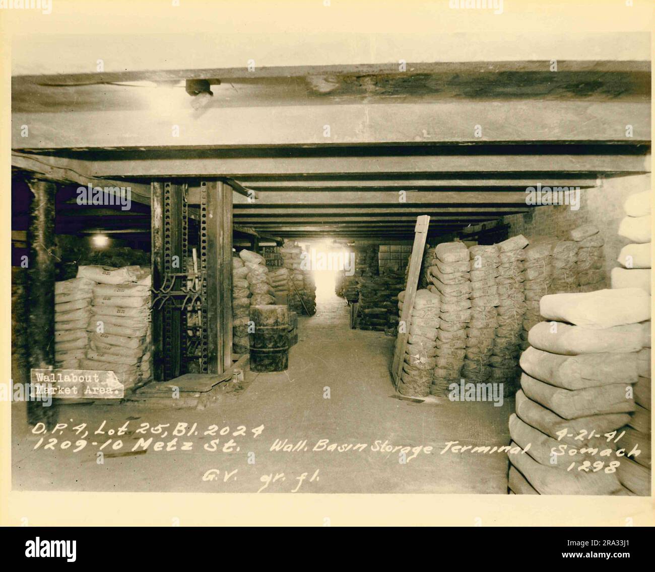 Foto des Wallabout Market, D.P. 4, Los 25, Gebäude 2024, 1209-10 Metz Streeet, Wand. Basin Storage Terminal, G.V. Erdgeschoss. Ansicht des großen Lagerbereichs mit Säckelstapeln und einem Ballenheber mit einem Eingangsbereich im Hintergrund, gedruckt von Negativ 1298. Stockfoto