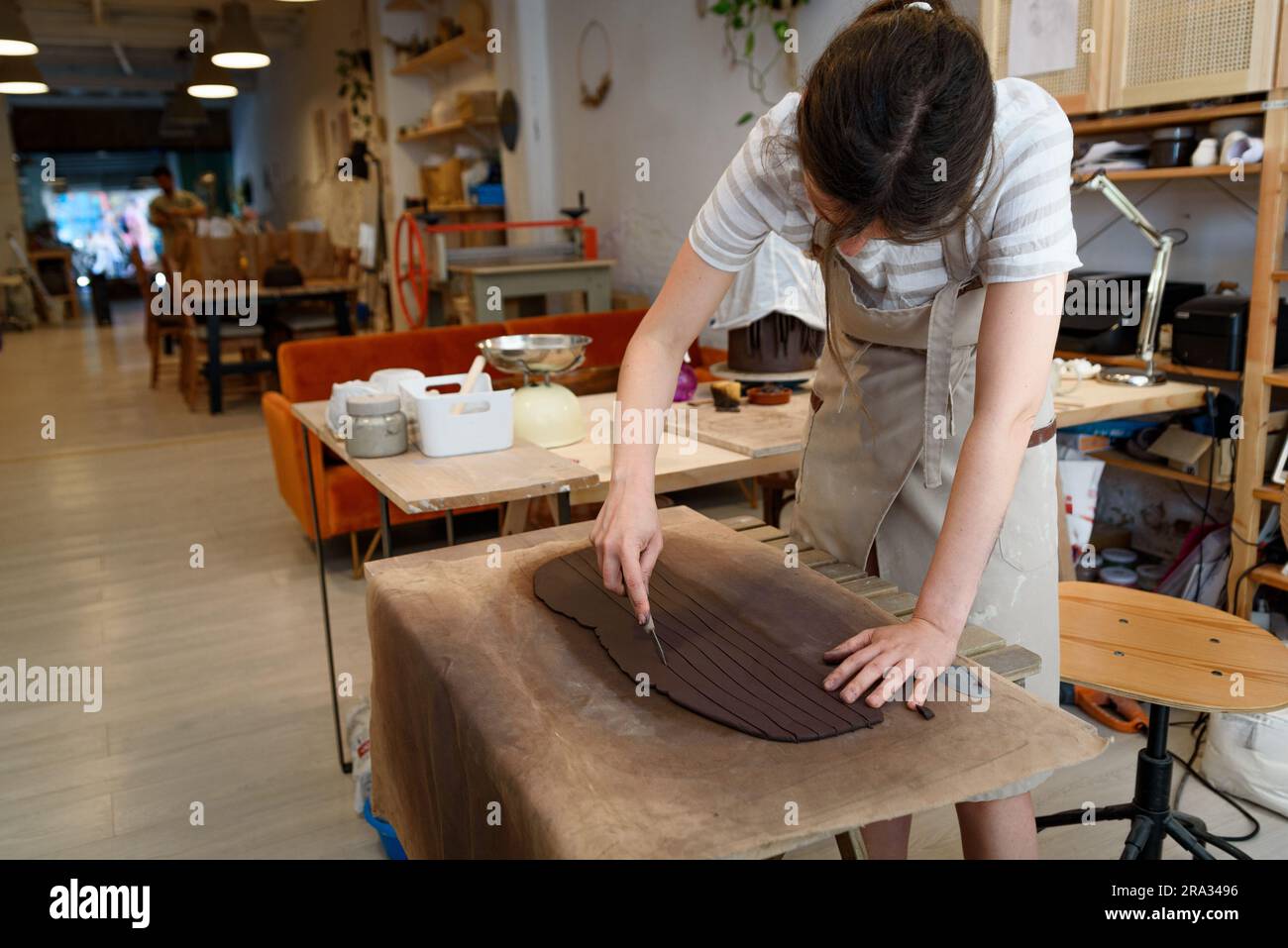 Frauenhände schneiden Keramik in Töpferwerkstatt und arbeiten rohe Keramikvase und Lehm, um Topf zu machen. Keramikwerkstatt mit natürlichem Licht zum Schaben, Glätten Stockfoto