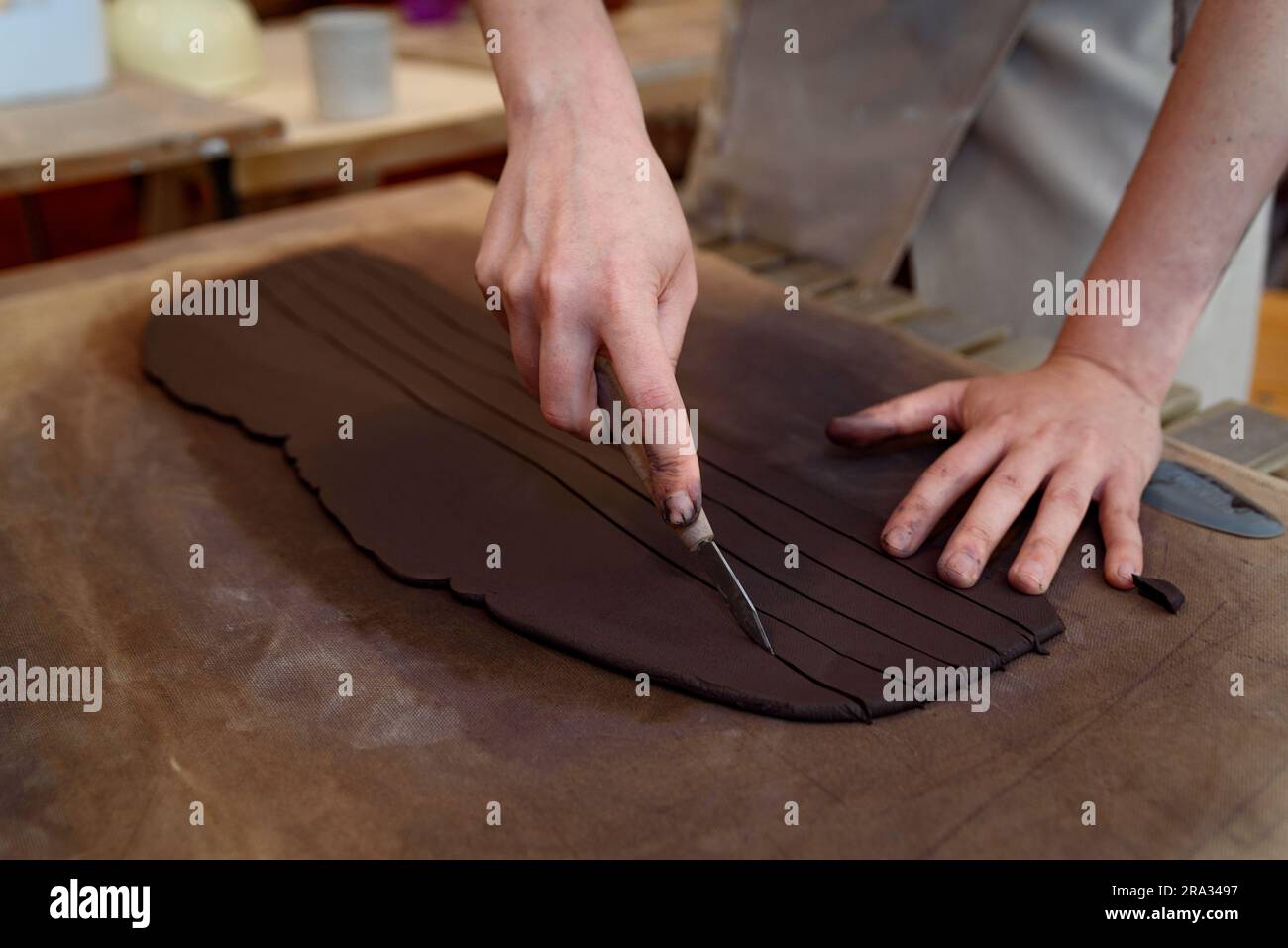 Frauenhände schneiden Keramik in Töpferwerkstatt und arbeiten rohe Keramikvase und Lehm, um Topf zu machen. Keramikwerkstatt mit natürlichem Licht zum Schaben, Glätten Stockfoto