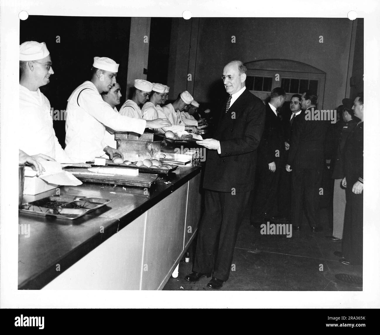 Foto von Mann, der Essen von Cafeteria Line erhält, serviert von Enlisted Men in Dress Whites. Stockfoto