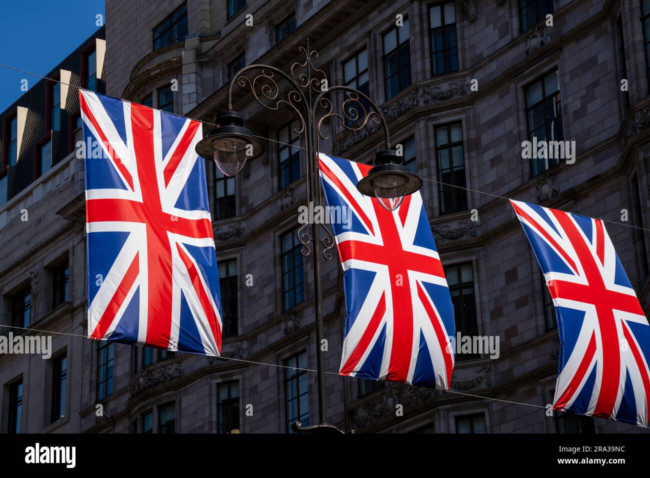 Die Union Jack Flaggen fliegen, hämmern, auf einer belebten Londoner Stadtstraße. Die roten, weißen und blauen britischen Flaggen sind ein Symbol der Freiheit und des Stolzes der Menschen. Stockfoto