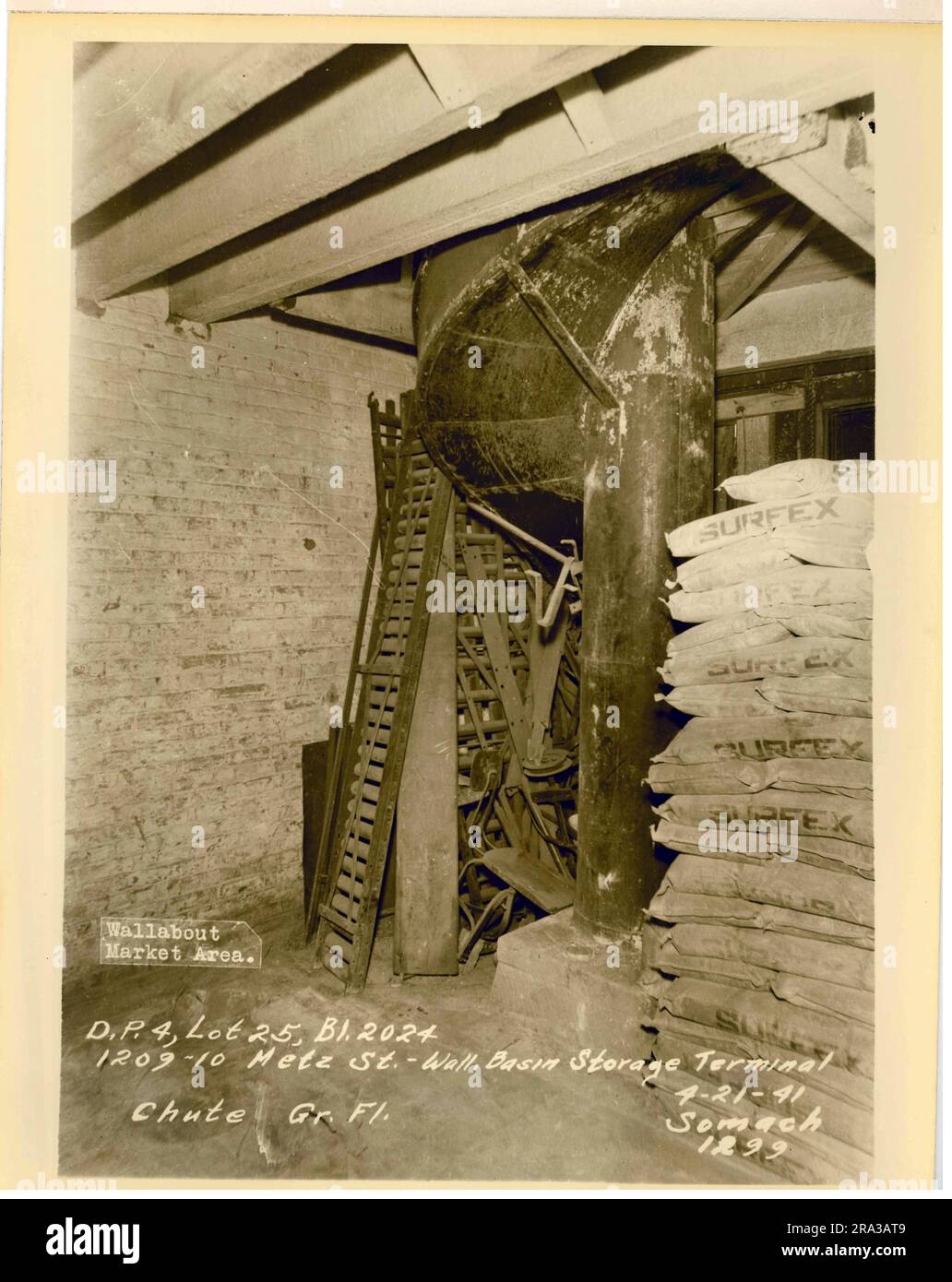 Foto des Wallabout Market, D.P. 4, Los 25, Bilding 2024, 1209-10 Metz Street, Wand. Becken-Stauraum Terminal Rutsche Erdgeschoss. Nahaufnahme der Außenansicht der gebogenen Rutsche von unten mit „Surfex“-beschrifteten Säcken in der Nähe, vom Negativ 1299... Stockfoto