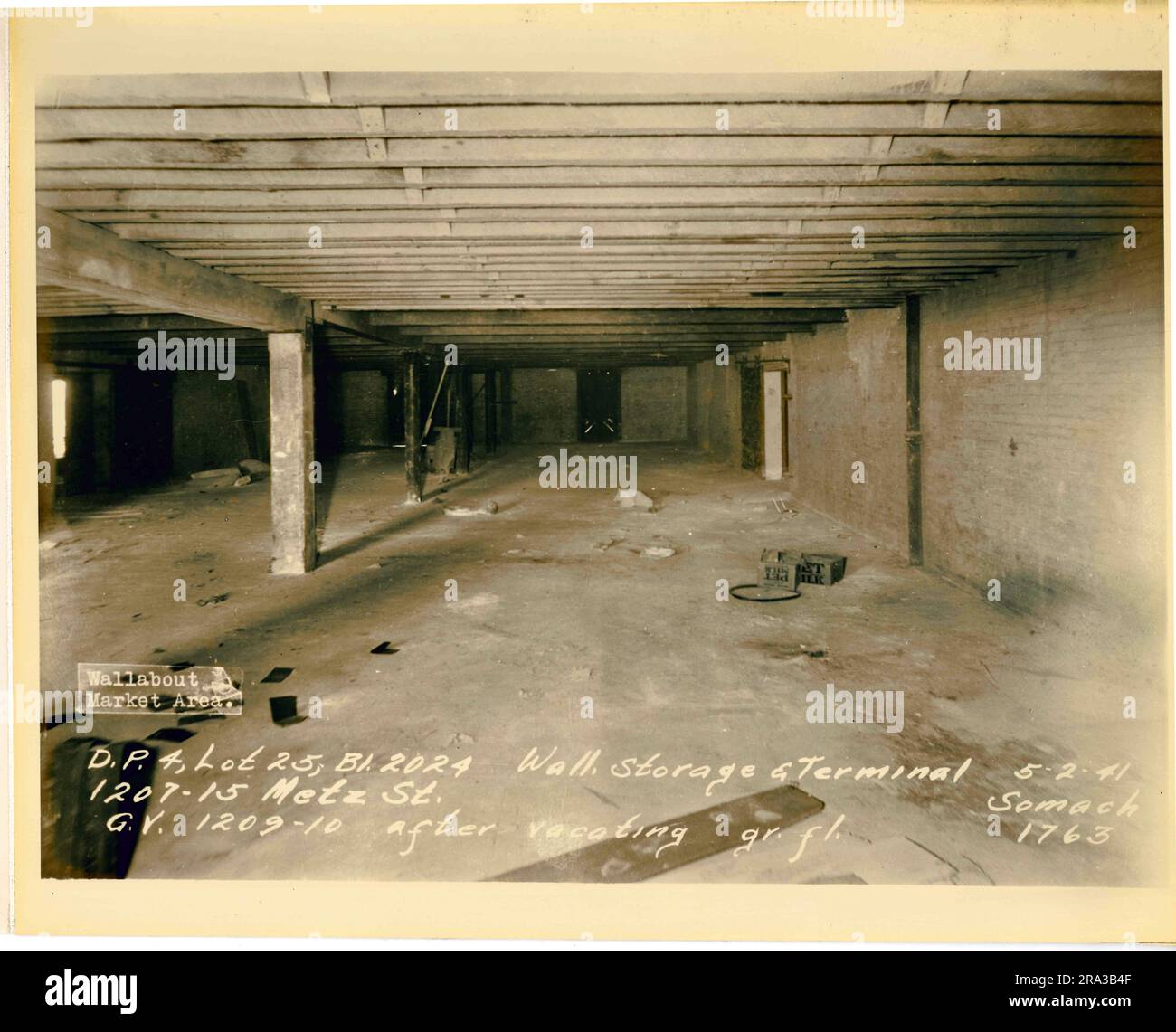 Foto des Wallabout Market, D.P. 4, Los 25, Gebäude 2024, 1207-15 Metz Street, Wand. Lagerterminal für Becken, G.V. 1209-10 nach der Verlegung, Erdgeschoss. Insgesamt widersprüchliche Ansicht des leeren Lagerplatzes mit Ziegelwänden und 2 Kisten für Haustiermilch auf dem Zementboden; gedruckt aus Negativdruck 1763. Stockfoto