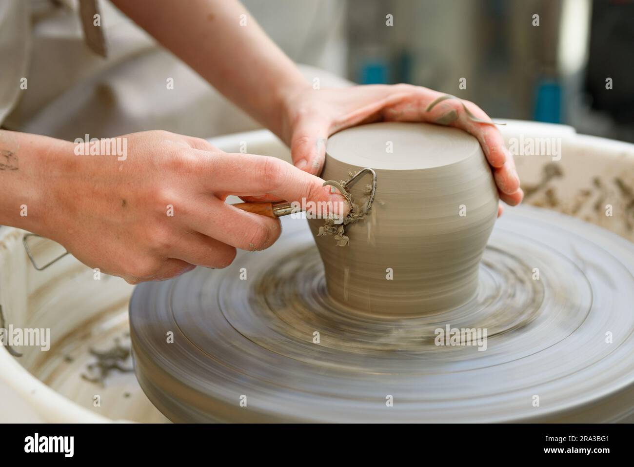 Nahaufnahme von roher Keramik, die auf der Drehmaschine oder dem Töpferrad läuft, mit Händen mit Werkzeug, die feine Details der Vase verfeinern Stockfoto