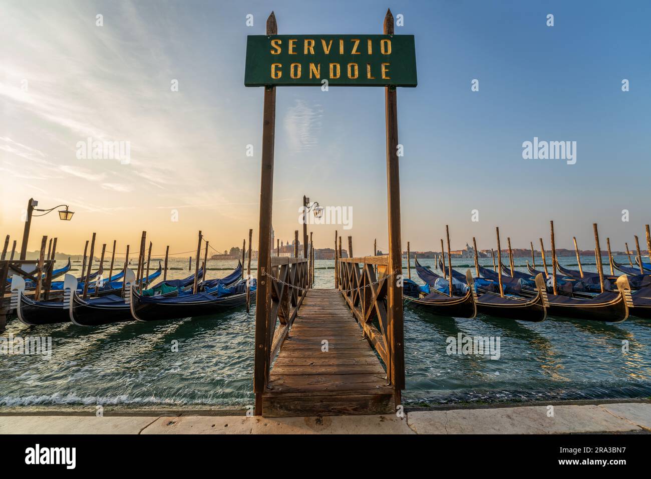 Gondeln, die am Pier mit dem Schild „Gondola Service“ bei Sonnenaufgang auf dem Kanal nahe dem Markusdom in Venedig, Italien, verankert sind. Diese italienische Skyline von Venedig ist unglaublich. Stockfoto