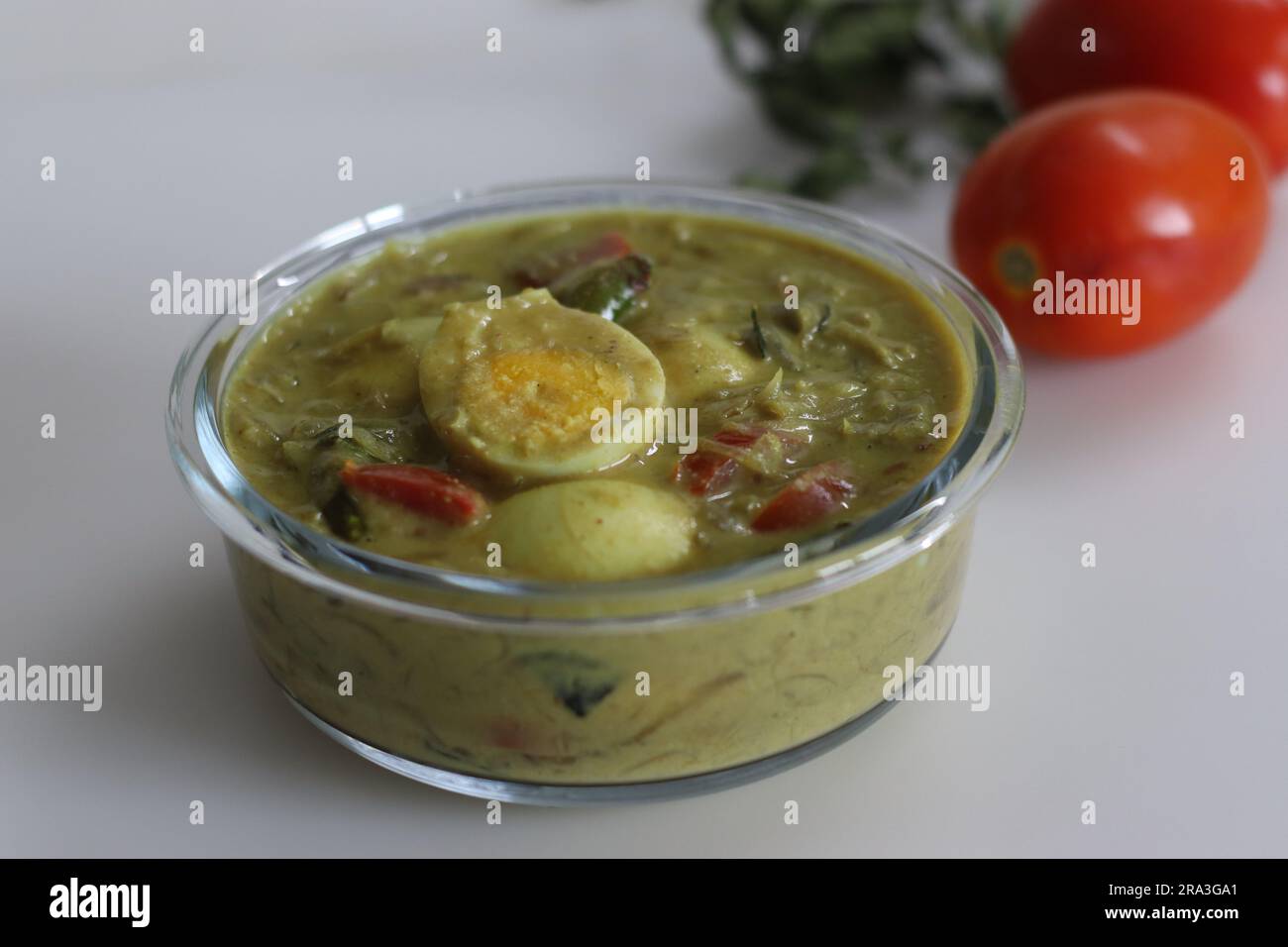 Eiercurry. Ei-Masala-Curry, zubereitet im Kerala-Stil mit Kokosmilch, Tomaten und Zwiebeln. Aufnahme auf weißem Hintergrund mit Tomaten und Curry l Stockfoto