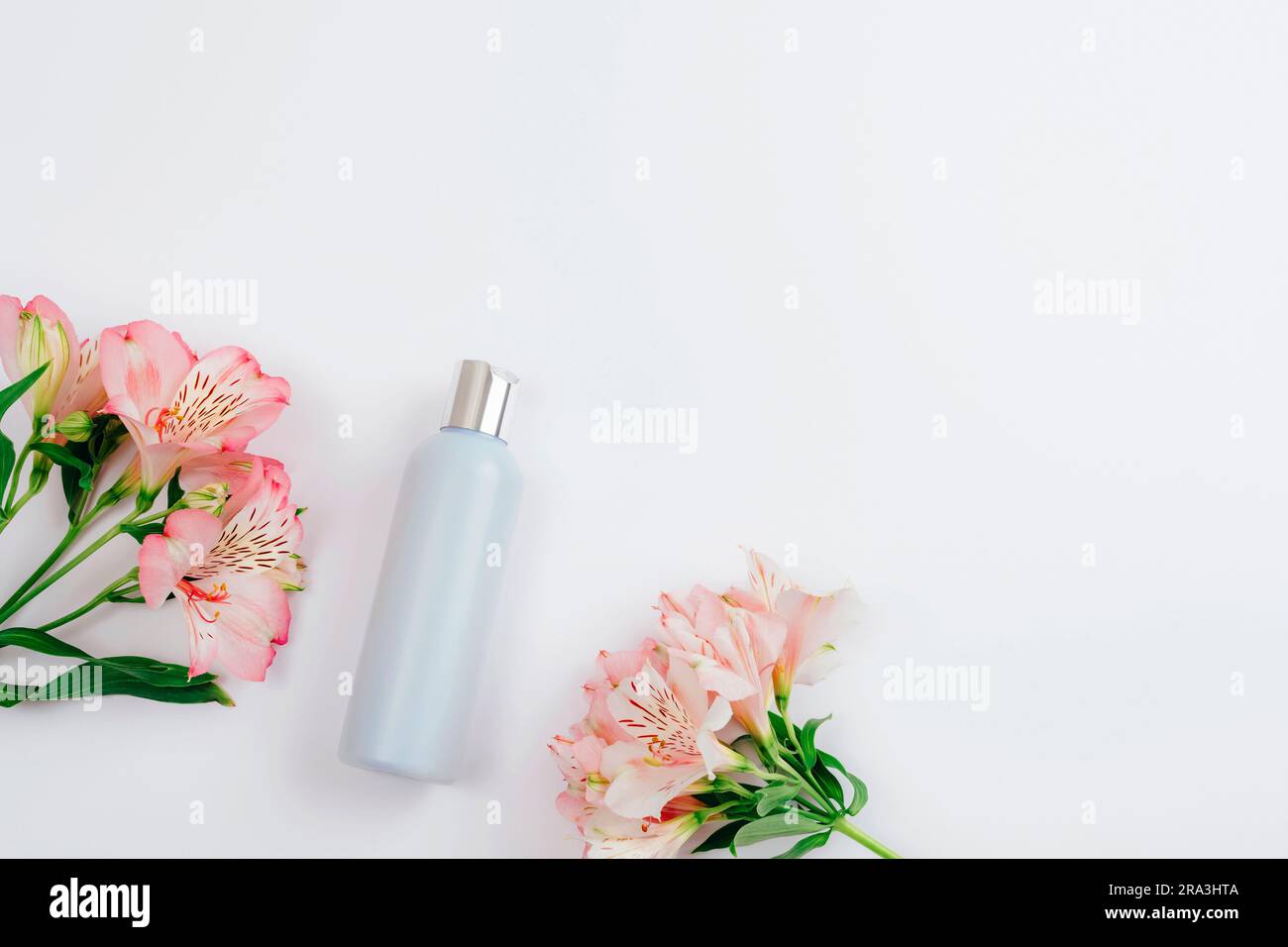 Blaue Kosmetikflasche und Alstroemeria Rosa Blumen auf weißem Hintergrund, flach liegend, Draufsicht. Leeres Label für Branding, Modell. Natürlicher ökologischer Kosmos Stockfoto