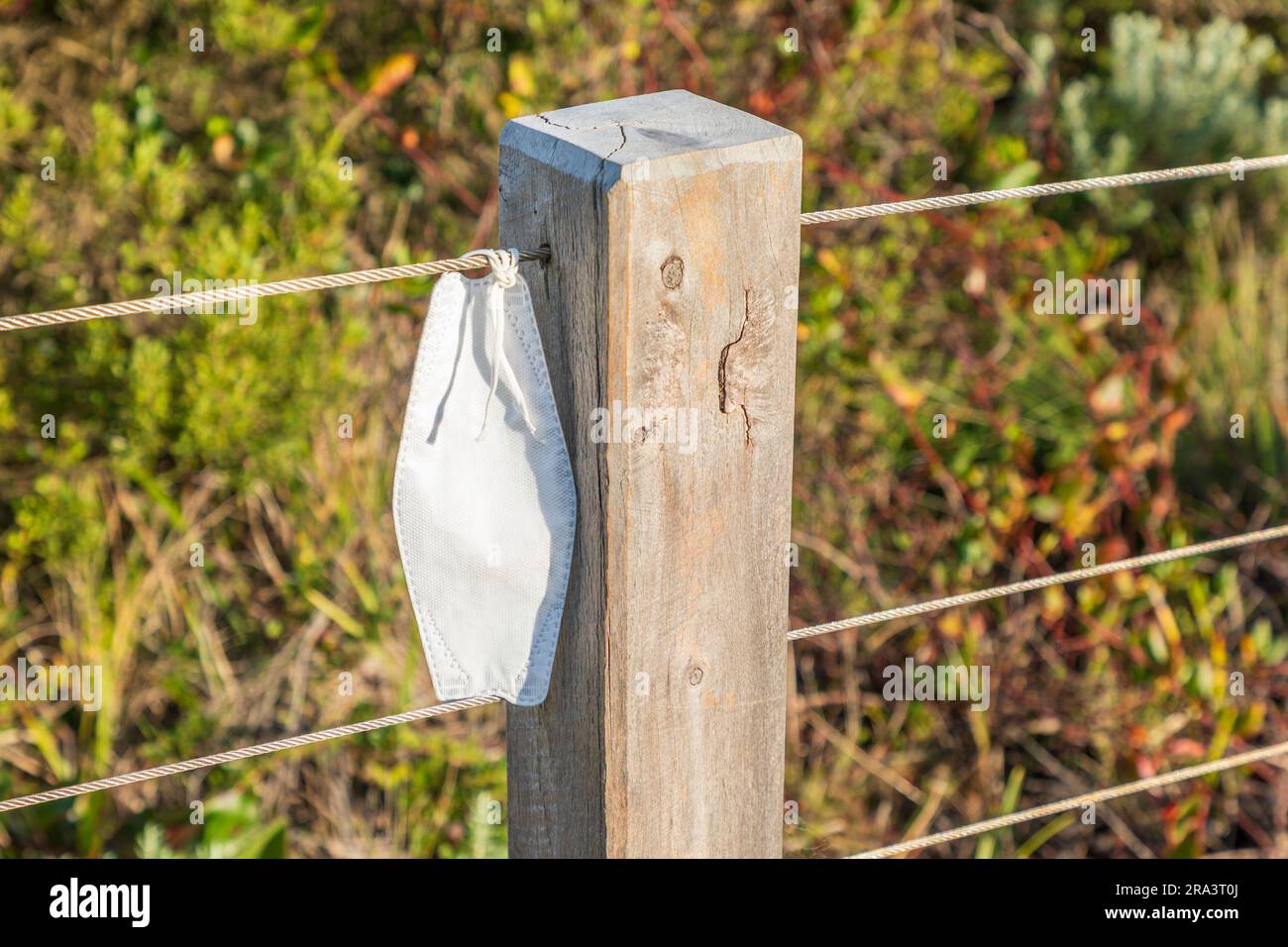 Foto einer coviden Gesichtsmaske, die an einem Zaun in der Nähe eines Holzpfeilers auf einem Wanderweg befestigt ist Stockfoto