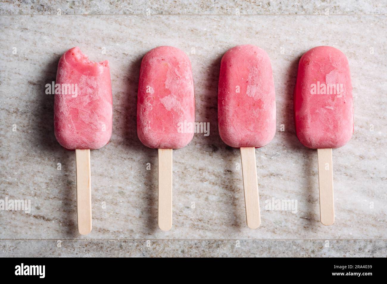 Erdbeerjoghurt-Eis am Stiel auf beigefarbenem Marmorhintergrund. Stockfoto