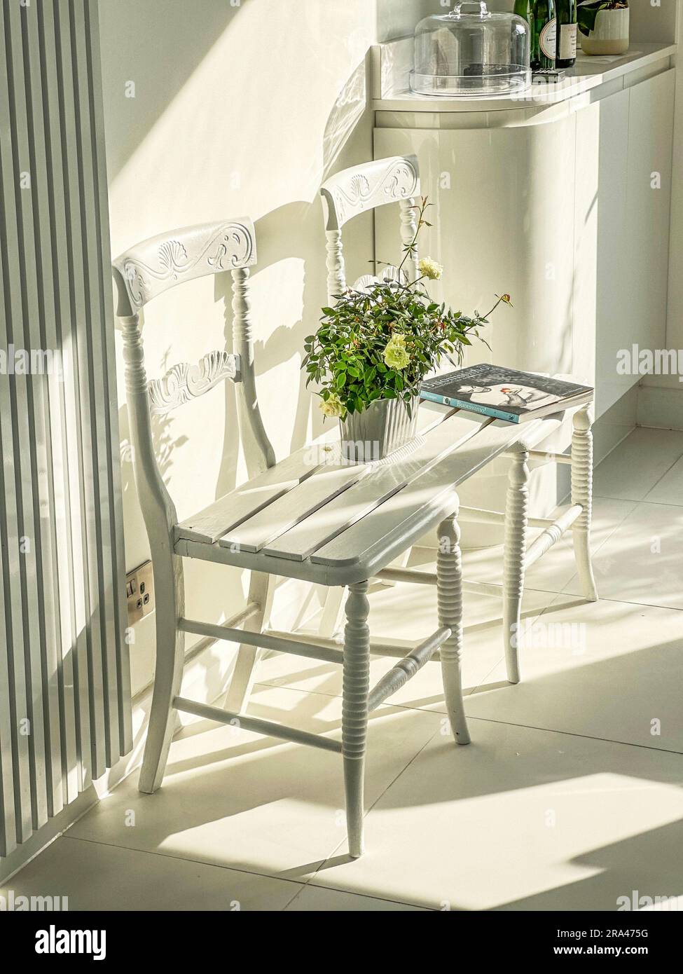Eine Sitzbank, die durch die Verbindung von zwei Stühlen in einer modernen, modernen weißen Küche hergestellt wird. (Ich habe keine Freigabe für das Buch auf dem Bild) Stockfoto