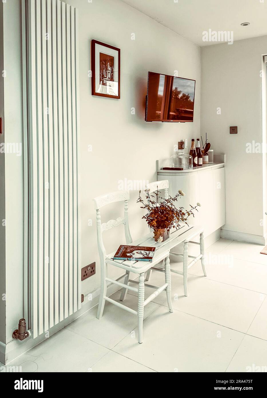 Eine Sitzbank, die durch die Verbindung von zwei Stühlen in einer modernen, modernen weißen Küche hergestellt wird. (Ich habe keine Freigabe für das Buch auf dem Bild) Stockfoto