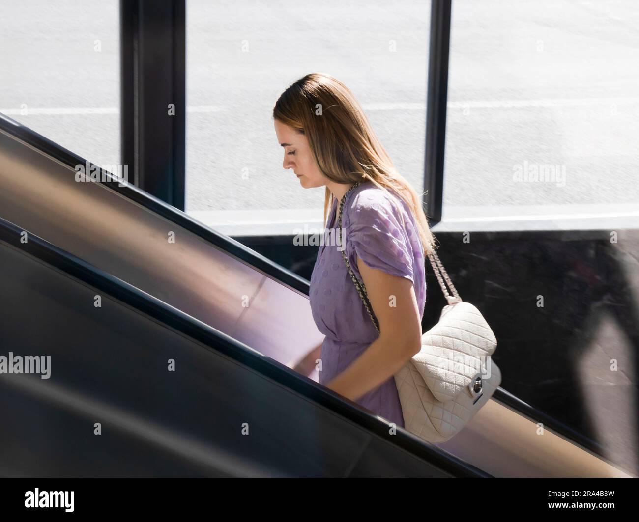 Belgrad, Serbien - 15. Juni 2022: Junge elegante Frau in lila Kleidung, die an einem sonnigen Tag auf die U-Bahn-Rolltreppe steigt Stockfoto