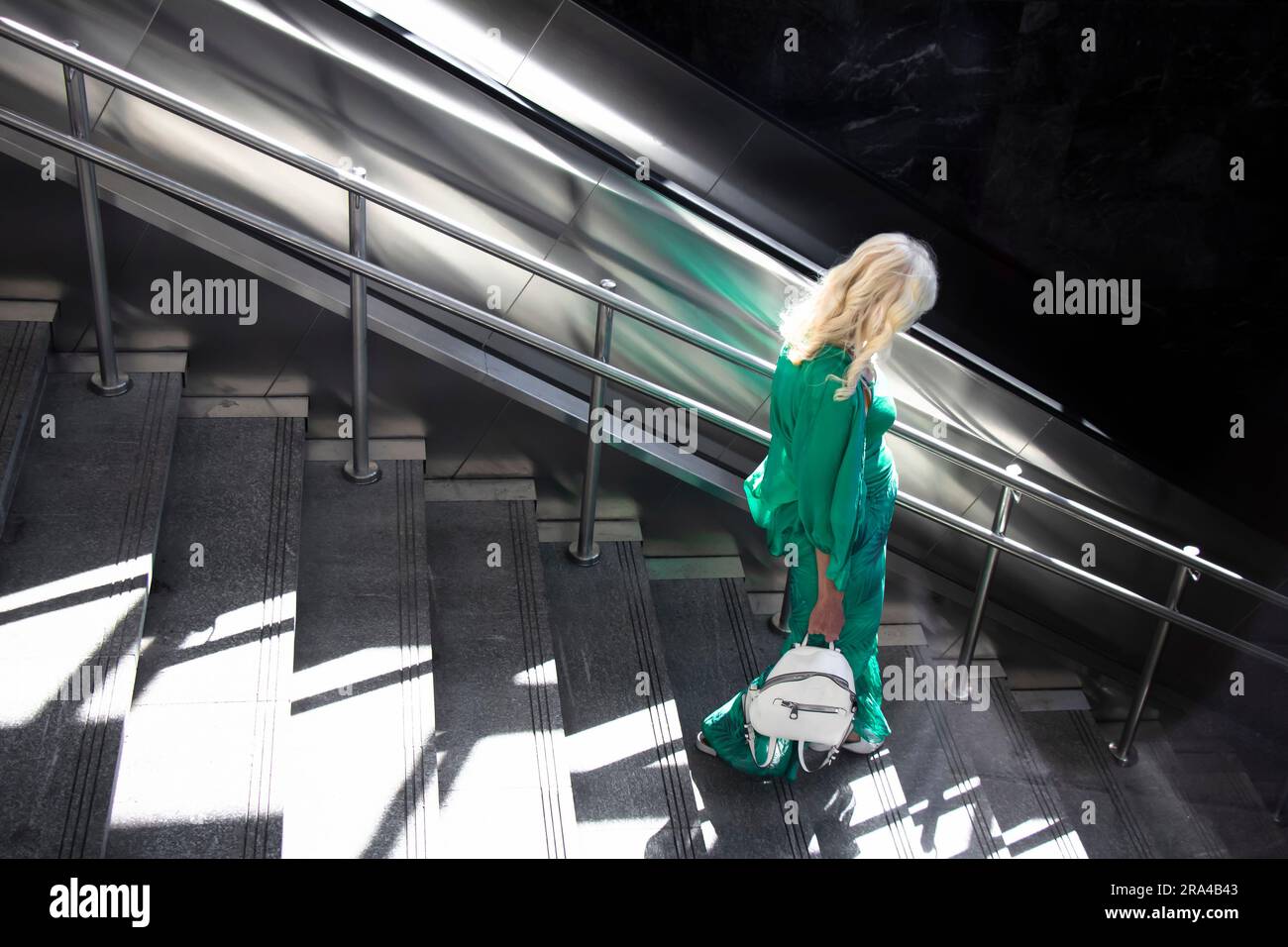 Belgrad, Serbien - 15. Juni 2022: Eine blonde Frau in grünem Outfit, die an einem sonnigen Tag die U-Bahn-Treppe hinuntergeht Stockfoto