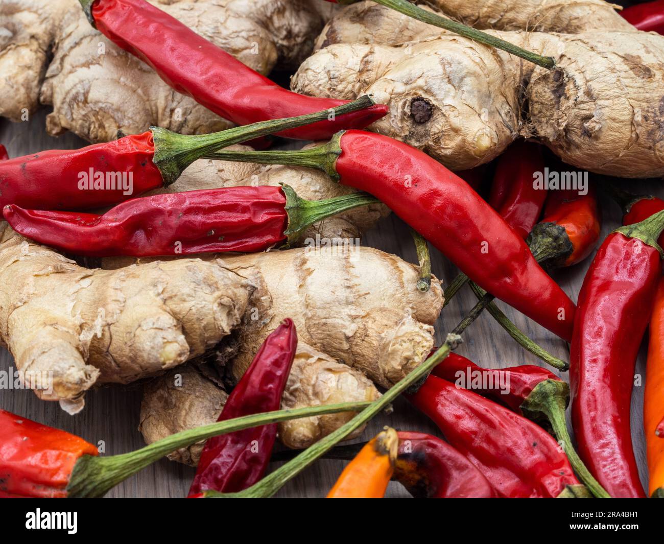 Ein Blick von oben auf Chili-Früchte in Rot- und Orangenfarben und Ingwer-Stücke im hölzernen Hintergrund. Stockfoto