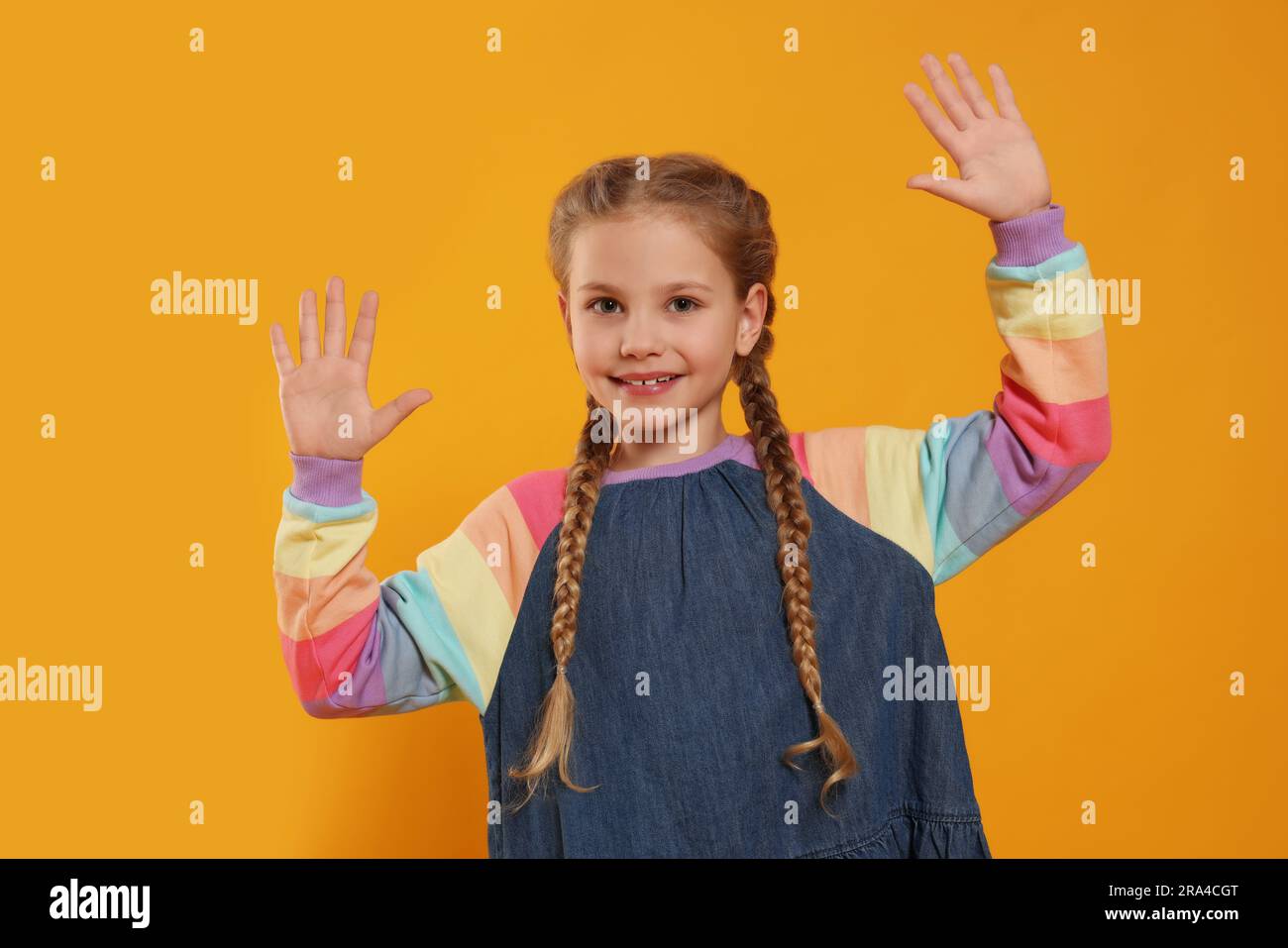 Glückliches Mädchen, das High Five gibt, mit beiden Händen auf orangefarbenem Hintergrund Stockfoto