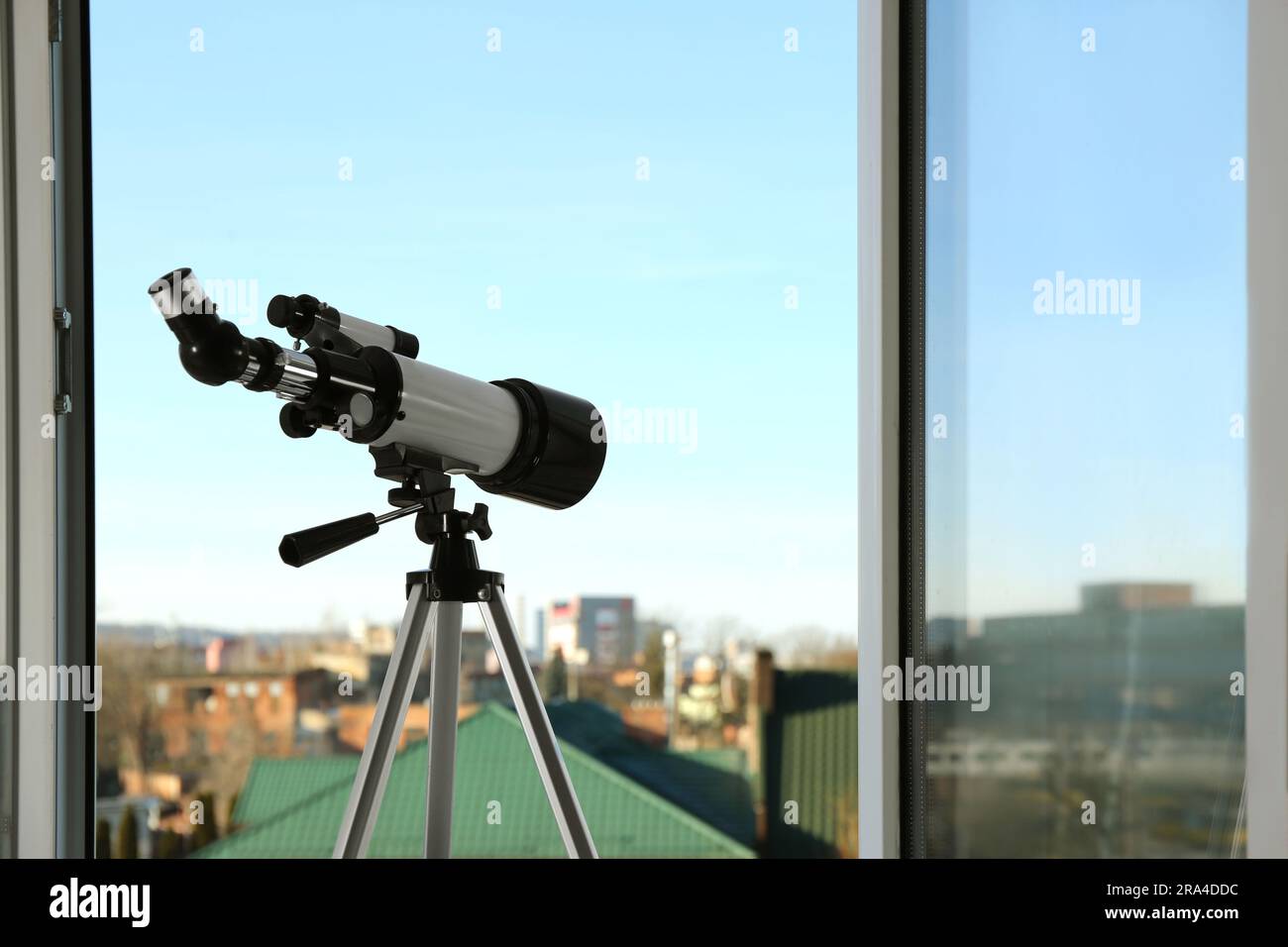 Stativ mit modernem Teleskop in der Nähe offener Fenster im Innenbereich. Platz für Text Stockfoto