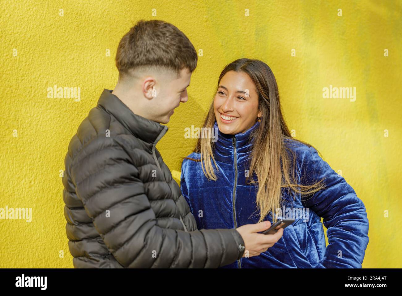 Ein lateinisches Mädchen, das mit einem weißen Jungen auf gelbem Hintergrund chattet. Stockfoto